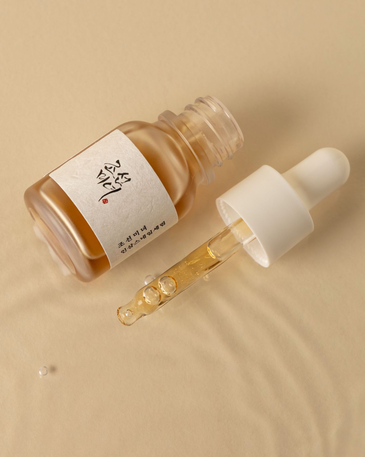 Glass dropper bottles containing golden beauty serum arranged in a minimalist composition on beige background.