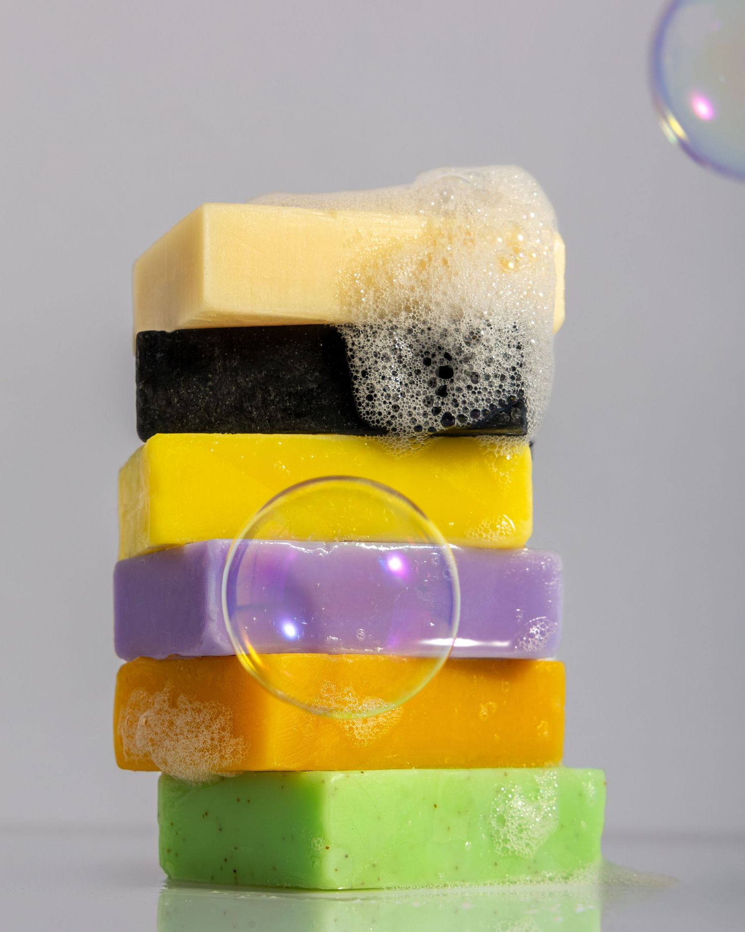 Stack of colorful handmade soap bars with bubbles against light background showing texture and variety.