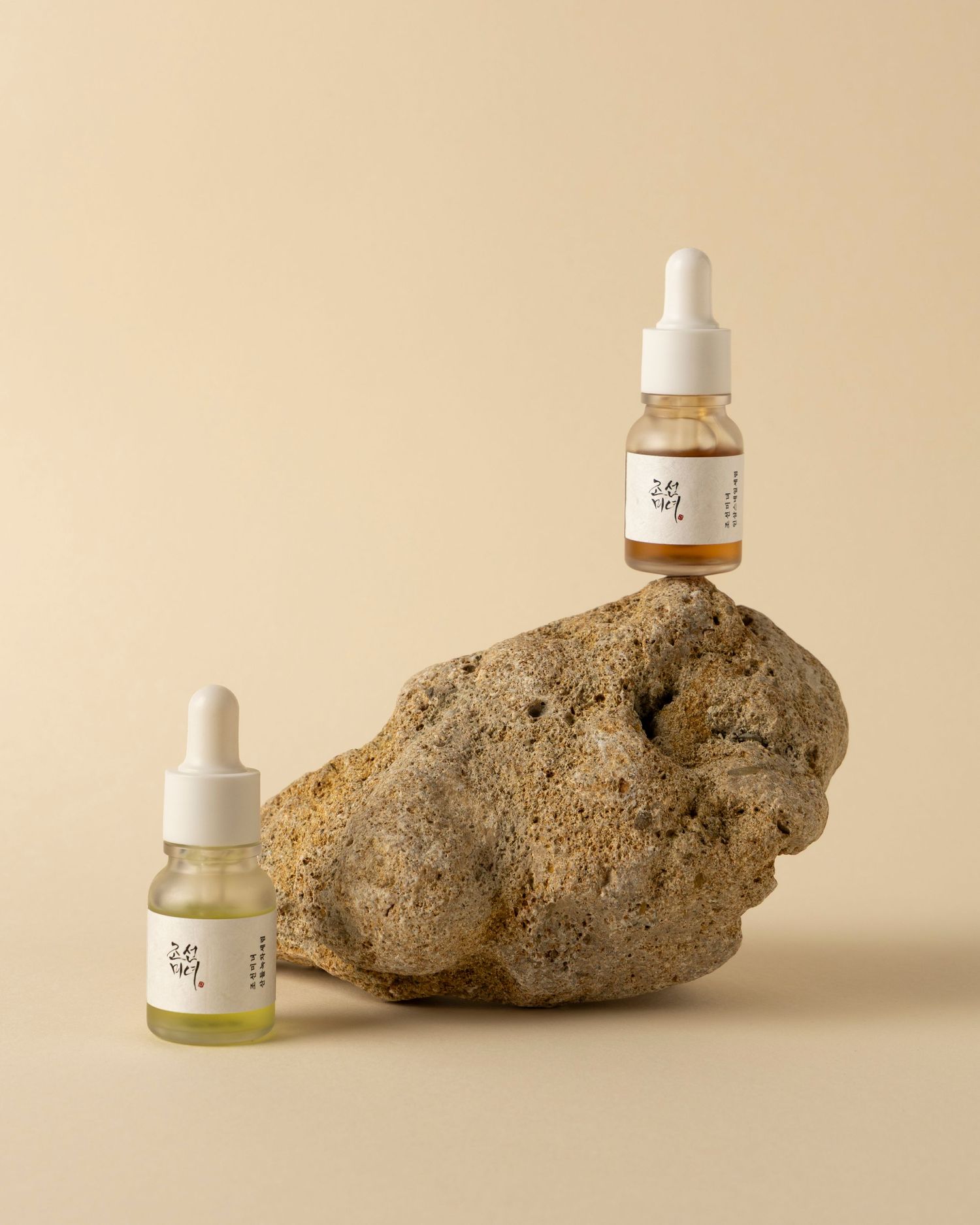 Minimalist product photography of skincare bottles with dropper caps displayed against natural stones on beige background.