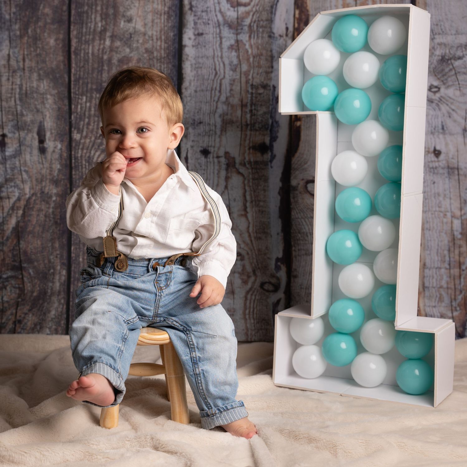 First birthday photo setup with large number one balloon arch in teal and white against rustic wood background.