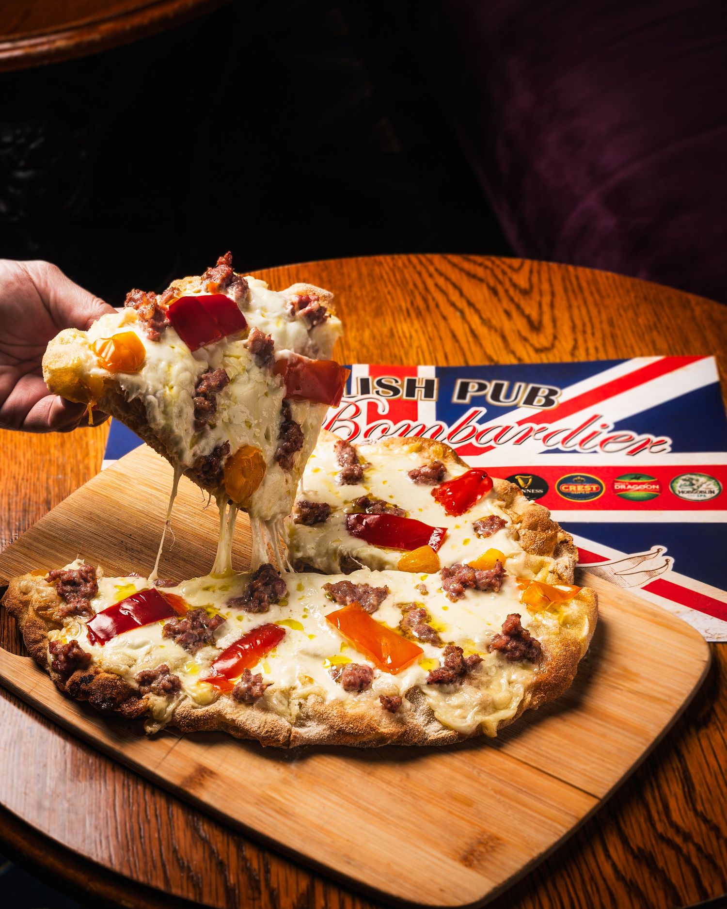 Cheesy pizza with melted mozzarella and toppings on wooden board next to American-themed packaging being served.