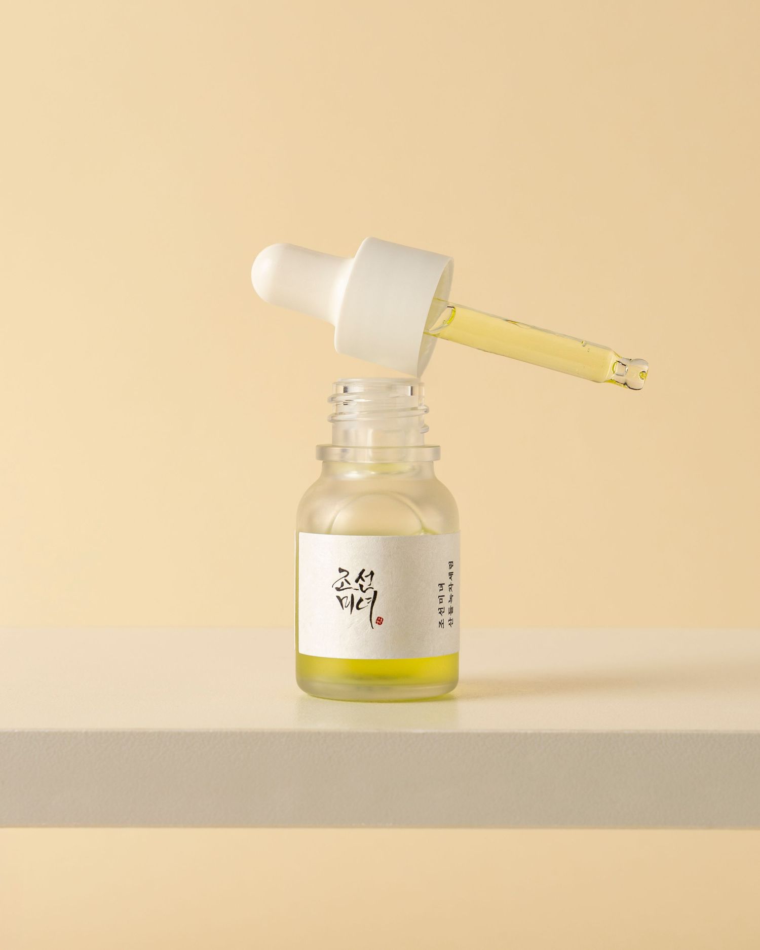 Small glass bottle with dropper containing yellow liquid serum against beige background.