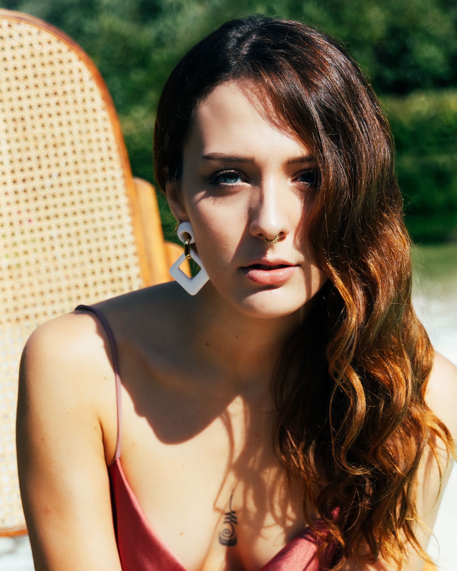 Woman in red top posing with warm sunlight against a textured woven background, creating dramatic shadows.