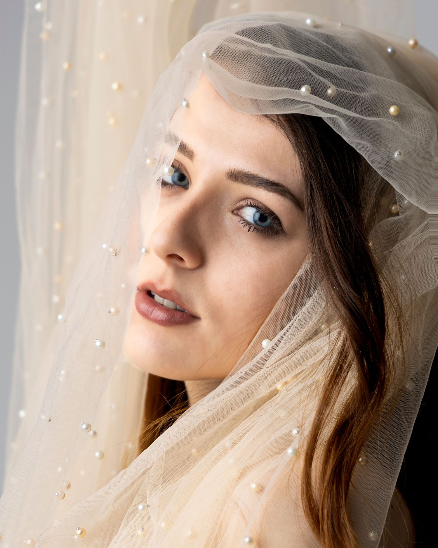 Bride wearing a pearl-embellished tulle veil with blue eyes and natural makeup, elegant bridal portrait.