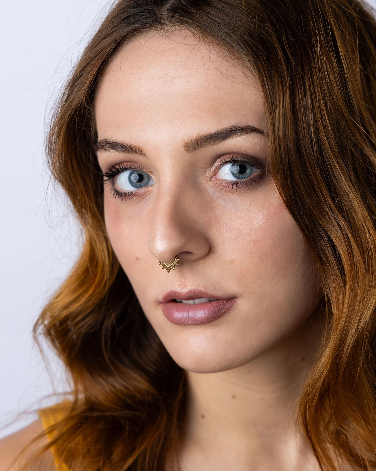 Studio beauty portrait with dramatic lighting showcasing gold glitter eye makeup and styled brown hair.