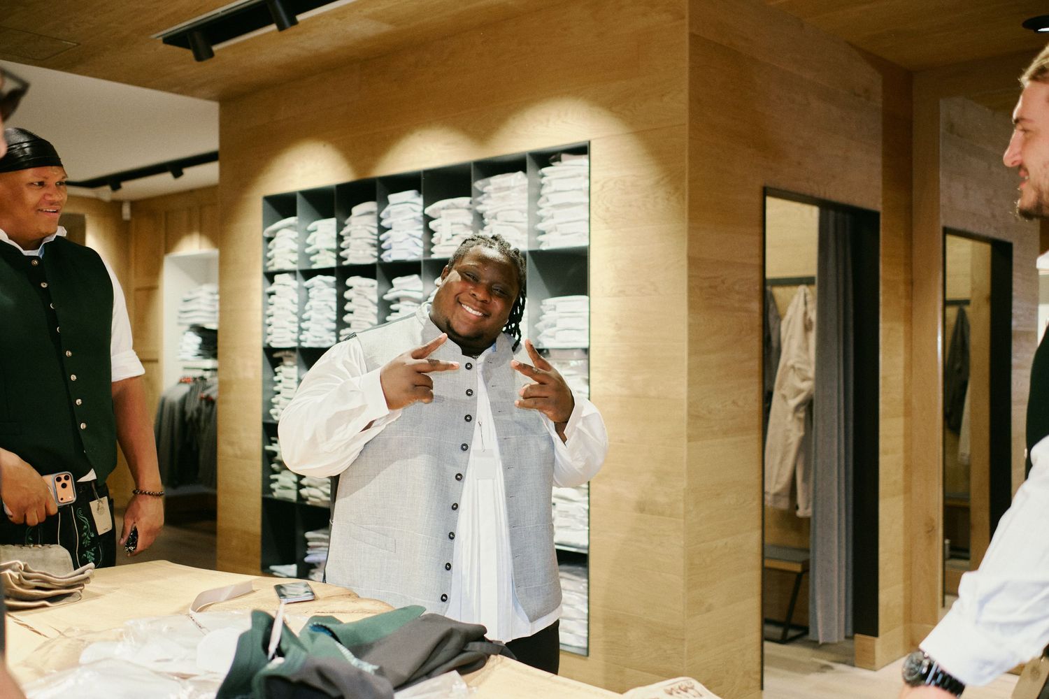 A man tries on a white button-up shirt in a modern clothing store with wooden shelves displaying folded garments.