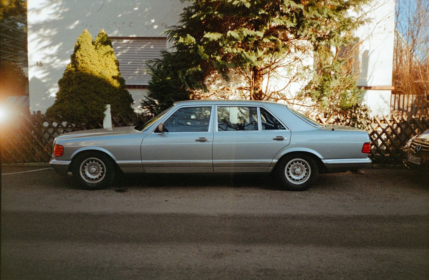 Silver classic Mercedes-Benz sedan parked on a driveway with trees and a house in the background.