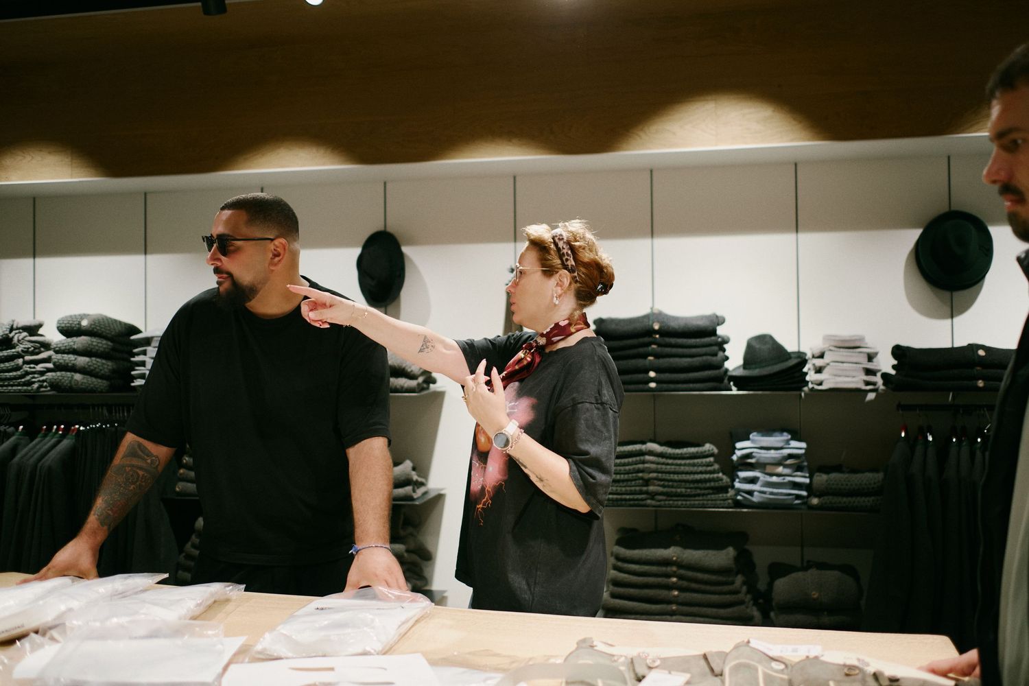 Two people discussing clothing options in a modern retail store with folded garments displayed on shelves.