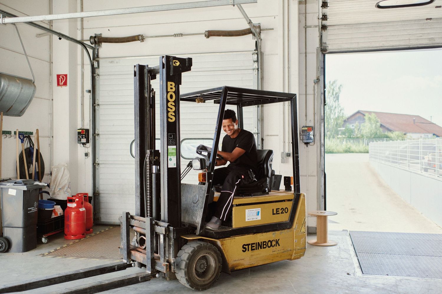Worker operating a Steinbock electric forklift inside an industrial warehouse with open garage doors.