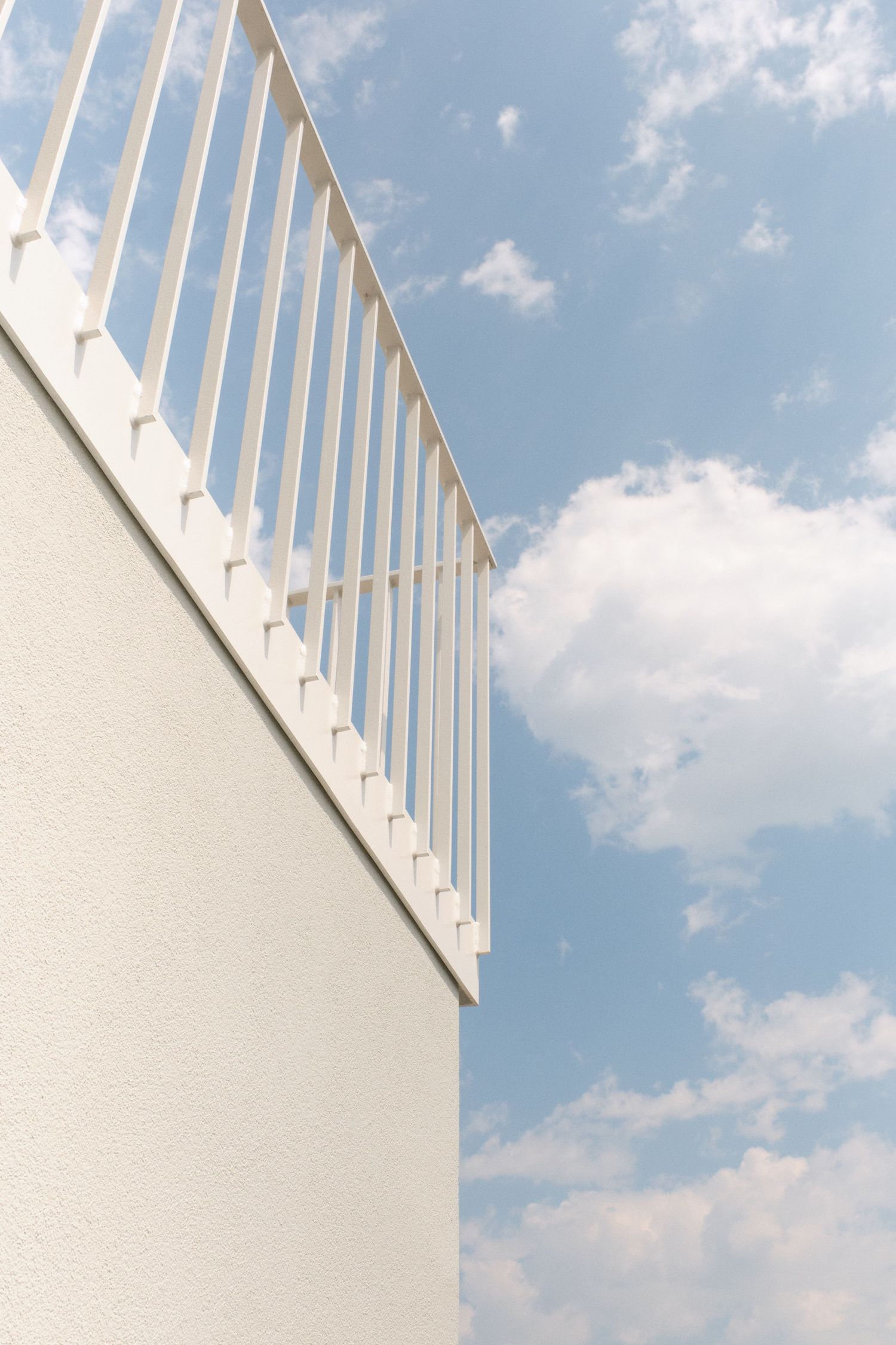 White metal railing on a building balcony against a blue sky with fluffy white clouds.