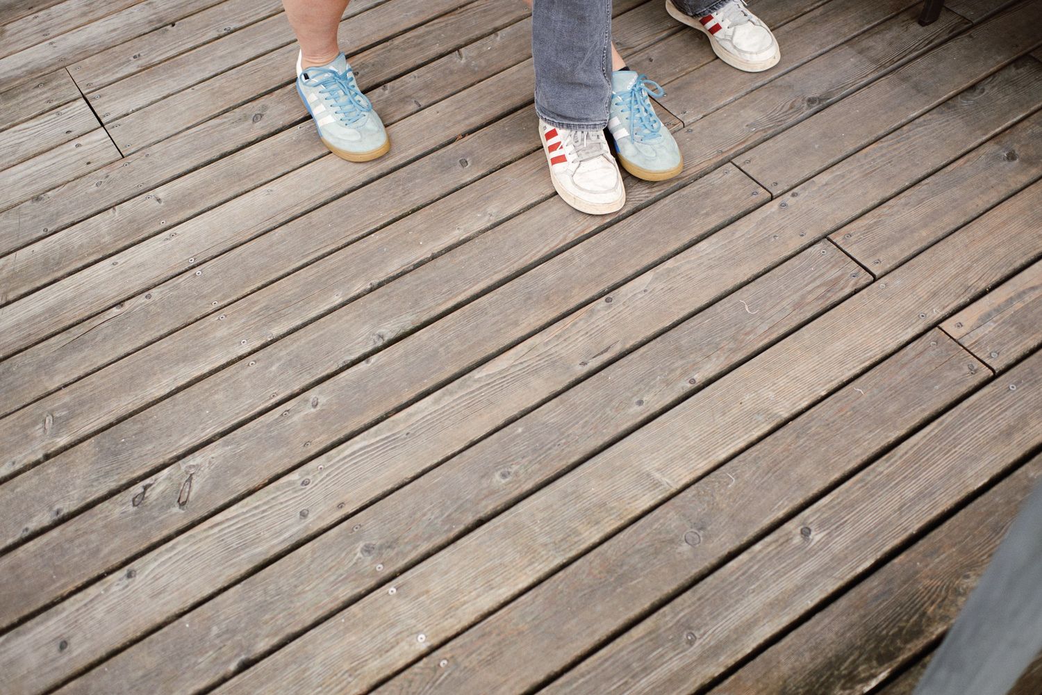 Two people wearing sneakers standing on a weathered wooden deck boardwalk.