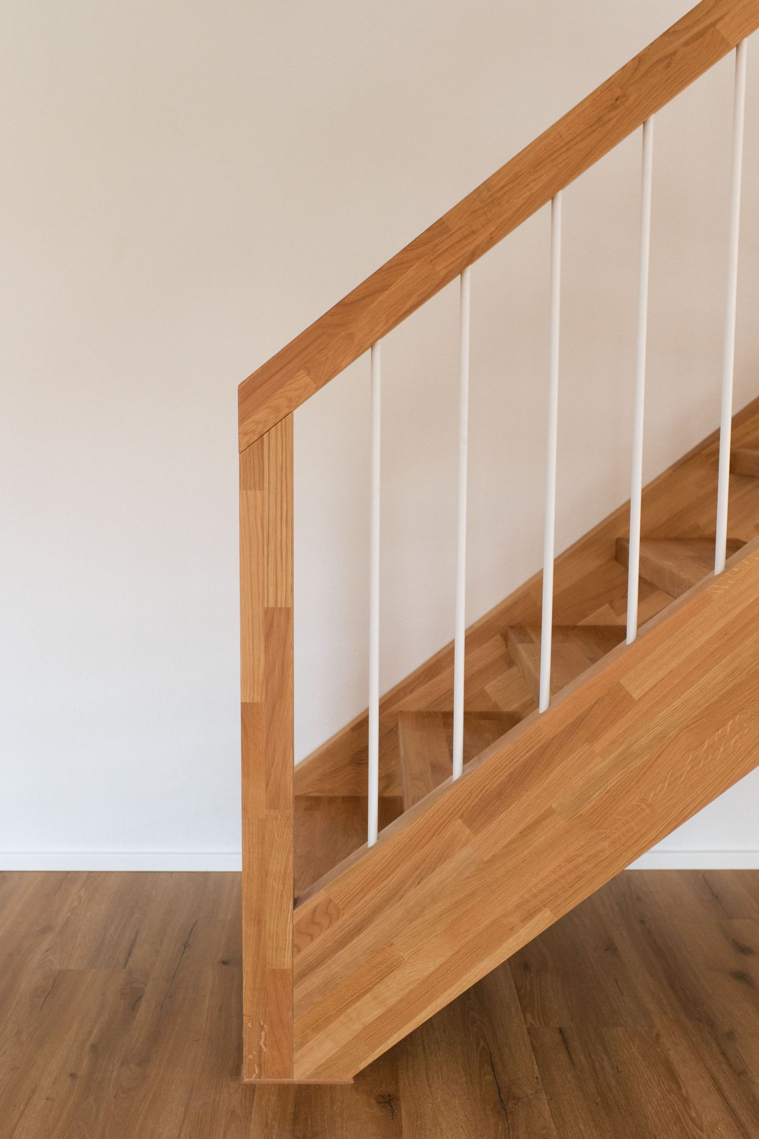 Modern wooden staircase with white metal balusters and oak handrail in a bright contemporary home interior.