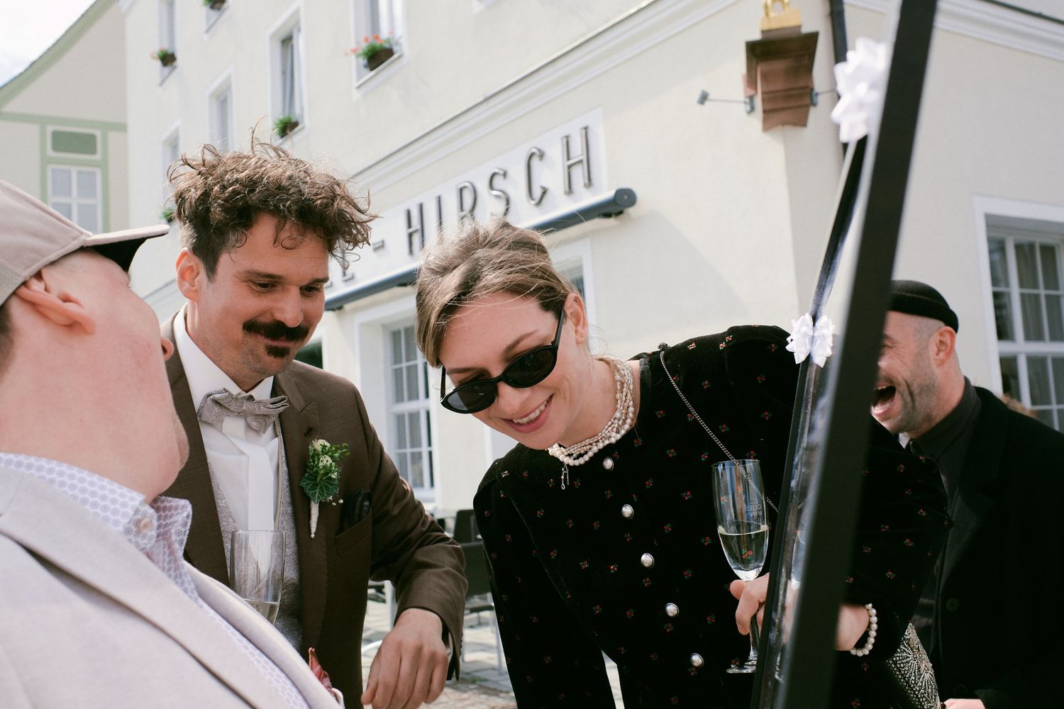 Elegantly dressed guests socializing outside Hirsch venue, woman in black velvet holding champagne glass at formal event.