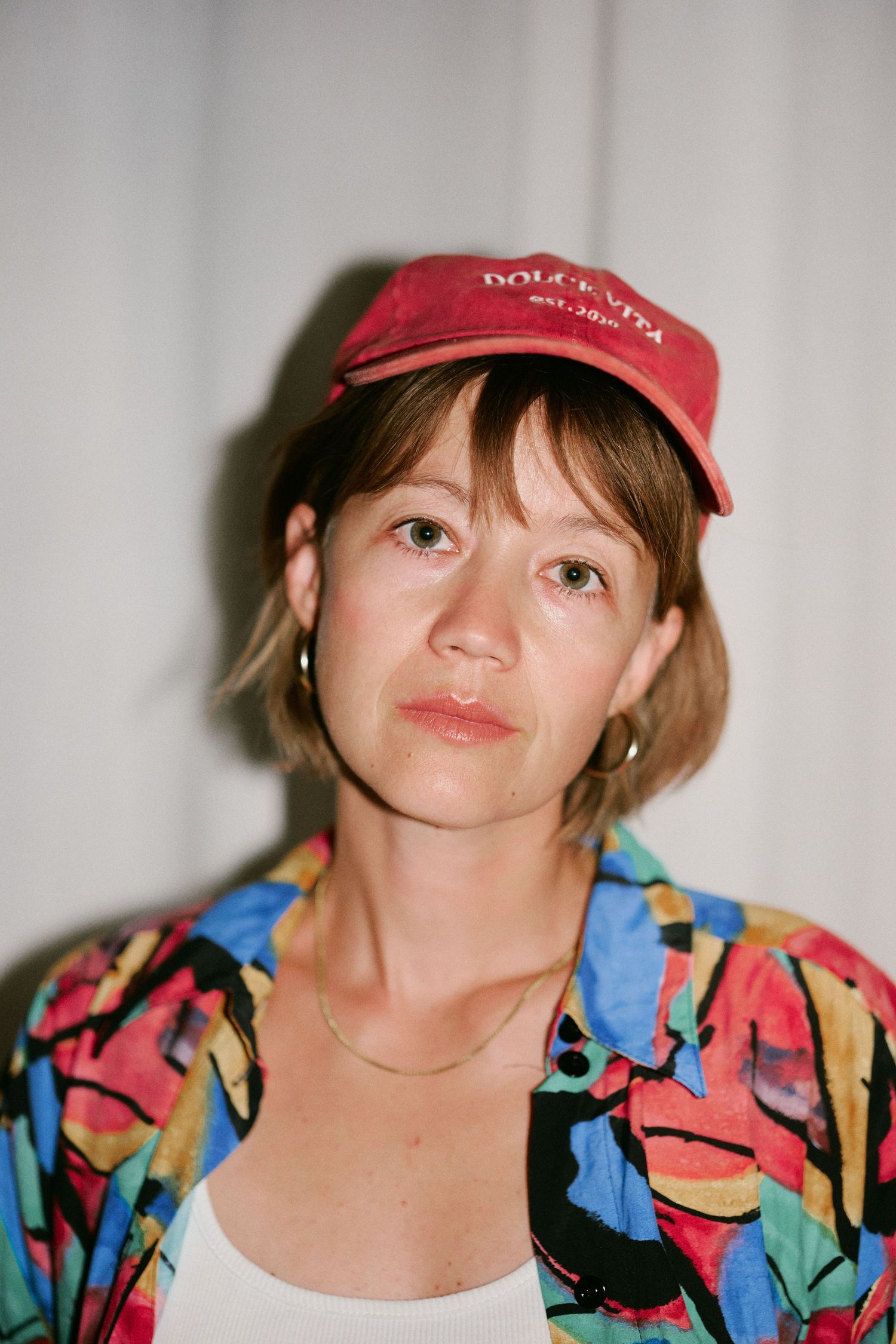 Woman wearing a red Dolce Vita cap and colorful abstract print blazer posing for a portrait photo.