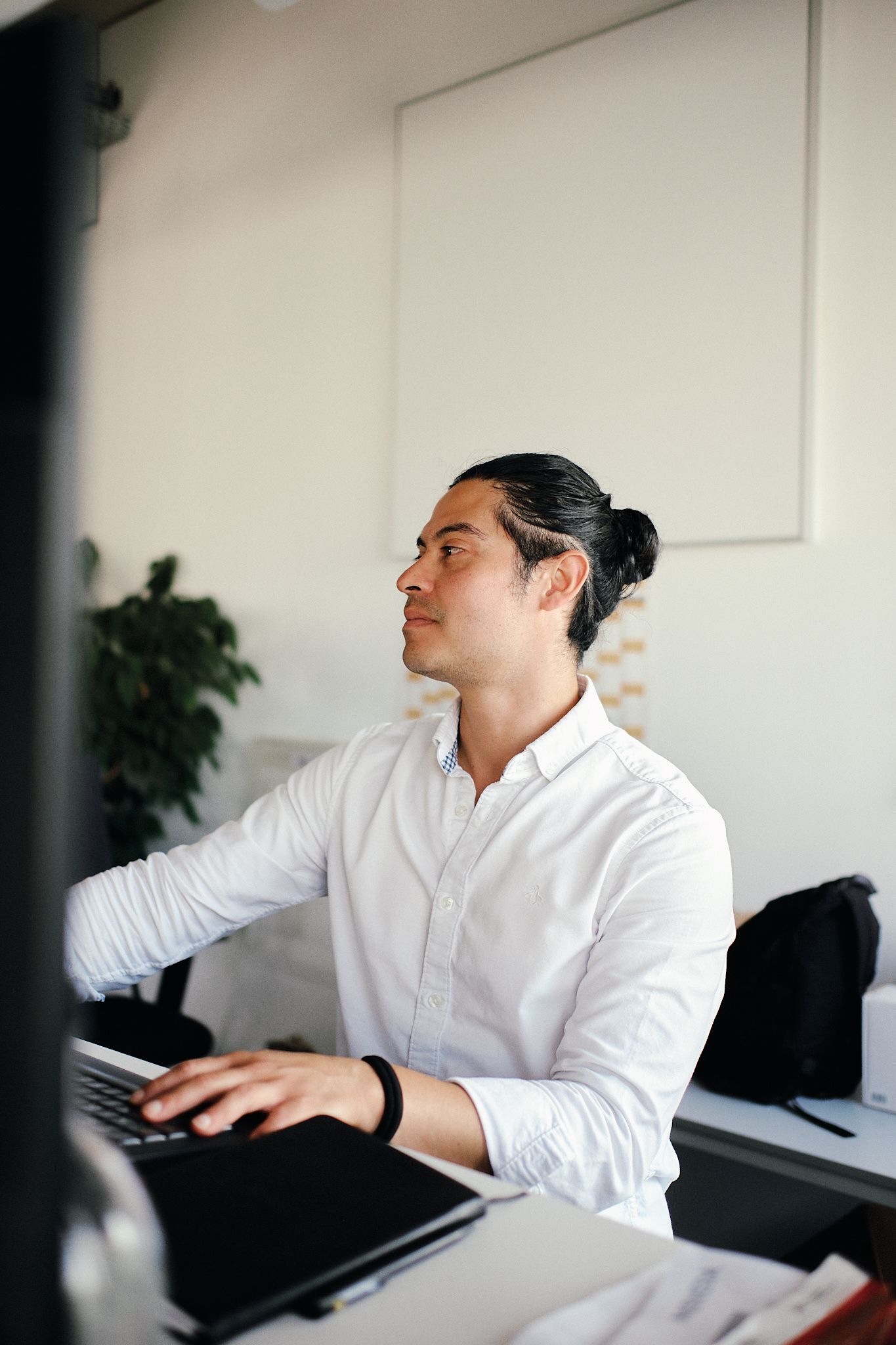 Young professional man in white shirt working at laptop in modern office, looking at computer screen.