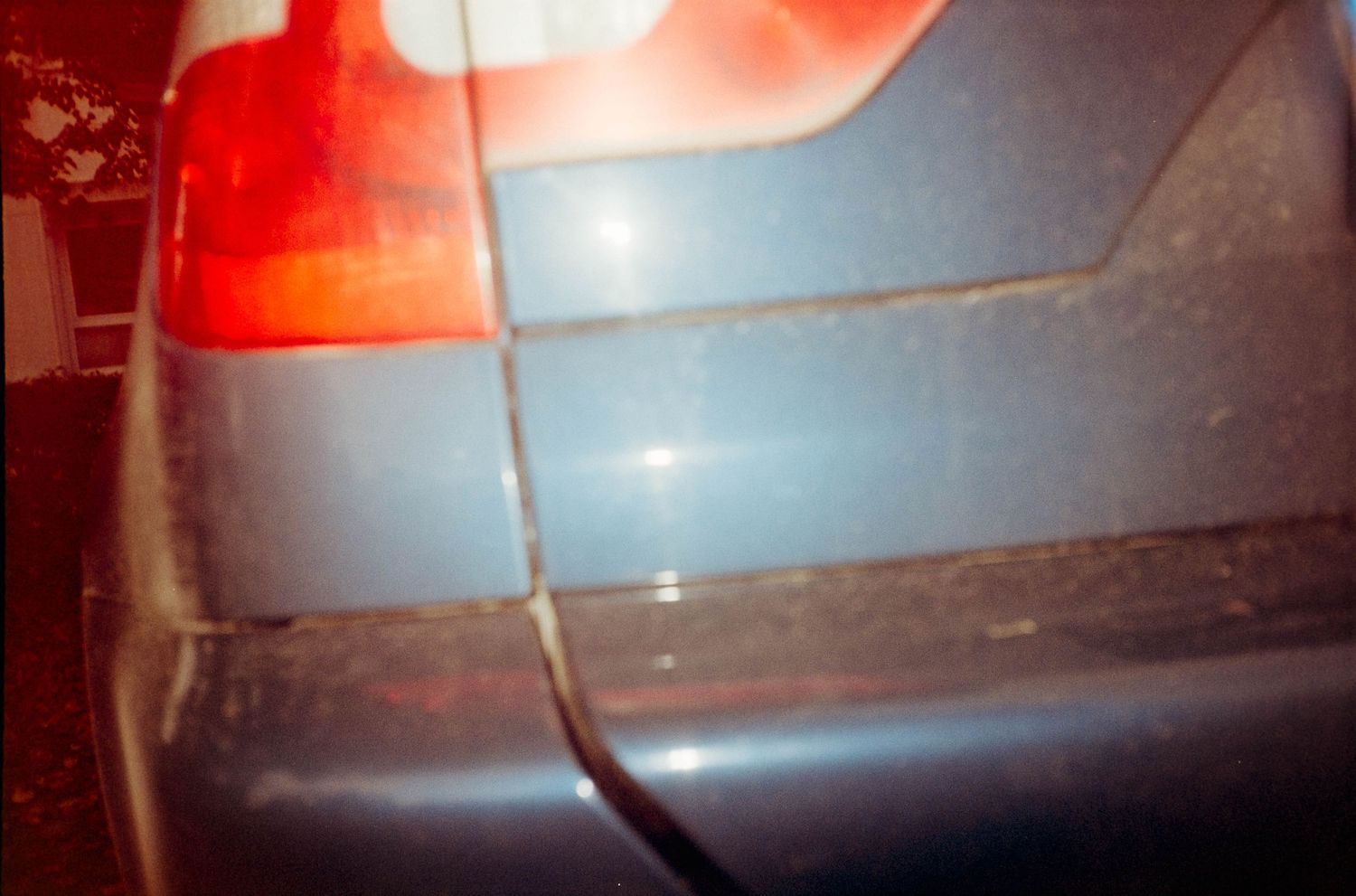 Close-up of a blue car rear bumper with red tail light visible, showing minor surface scratches and dirt.