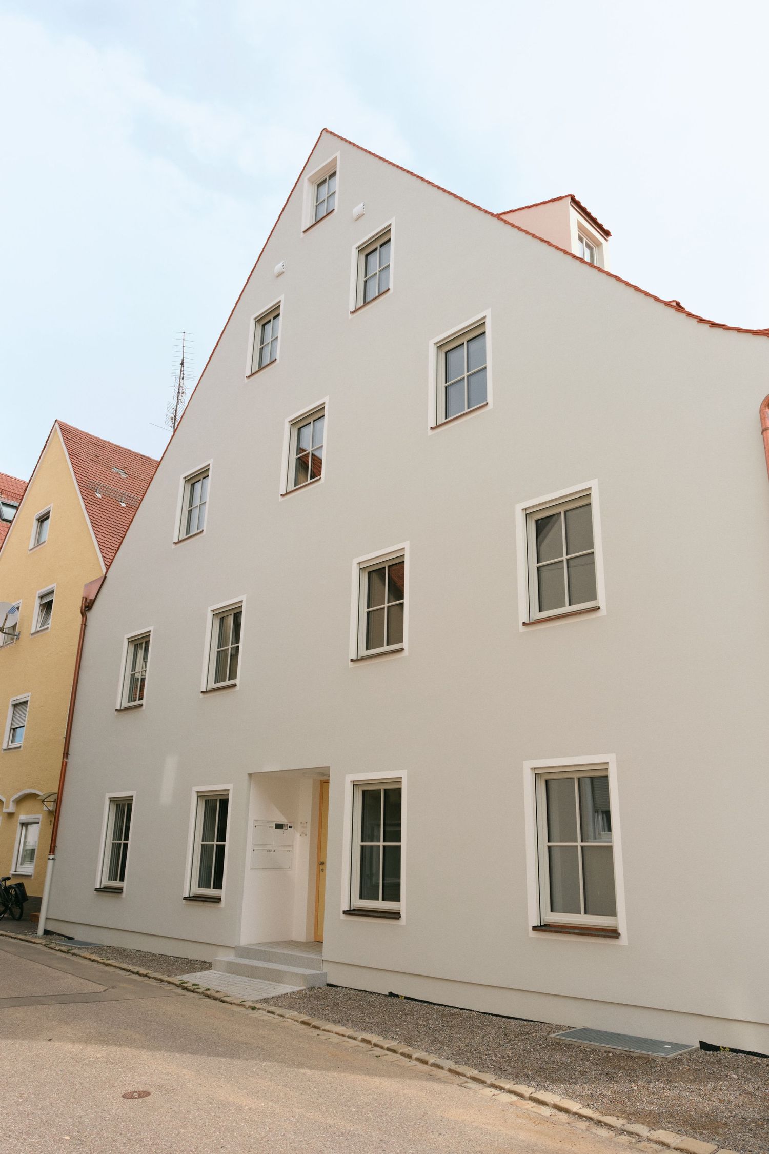 White multi-story European building with symmetrical windows on a cobblestone street in a historic town.
