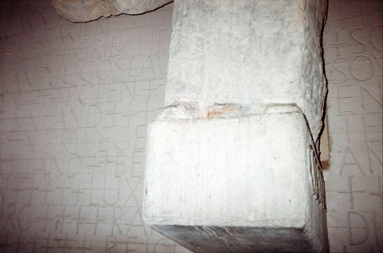 Ancient stone pillar with carved Latin inscriptions on weathered marble walls in historic archaeological site.