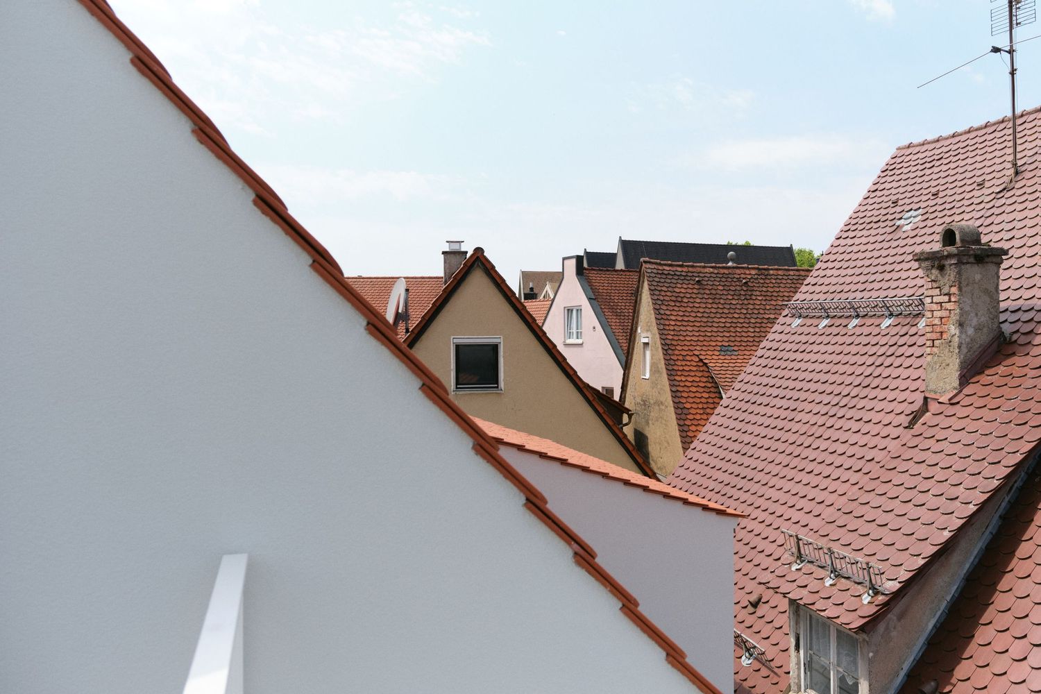 Aerial view of red terracotta tiled rooftops and white building facades in a European town under a blue sky.