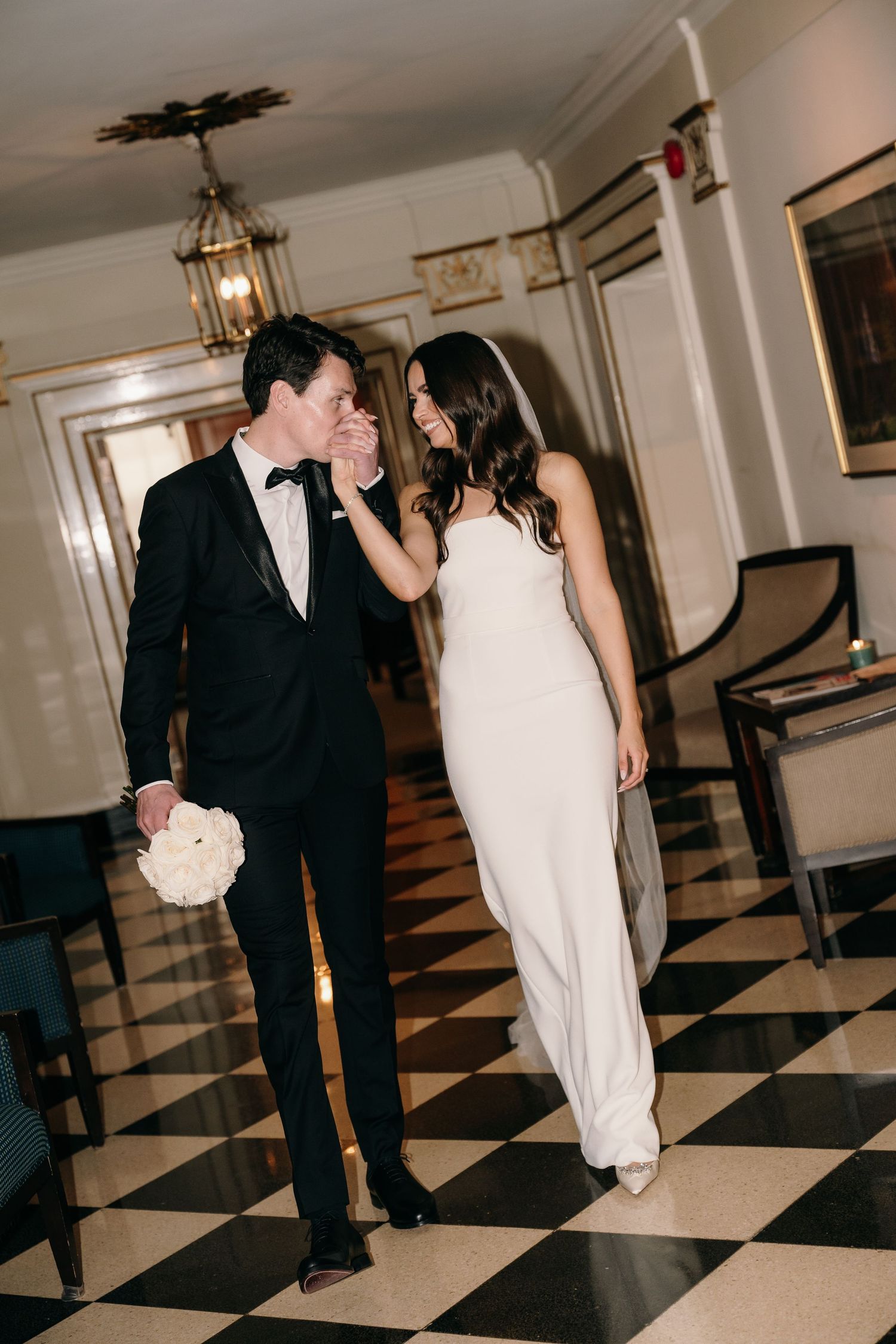 Bride and groom sharing a tender moment walking on black and white checkered marble floor in grand venue.
