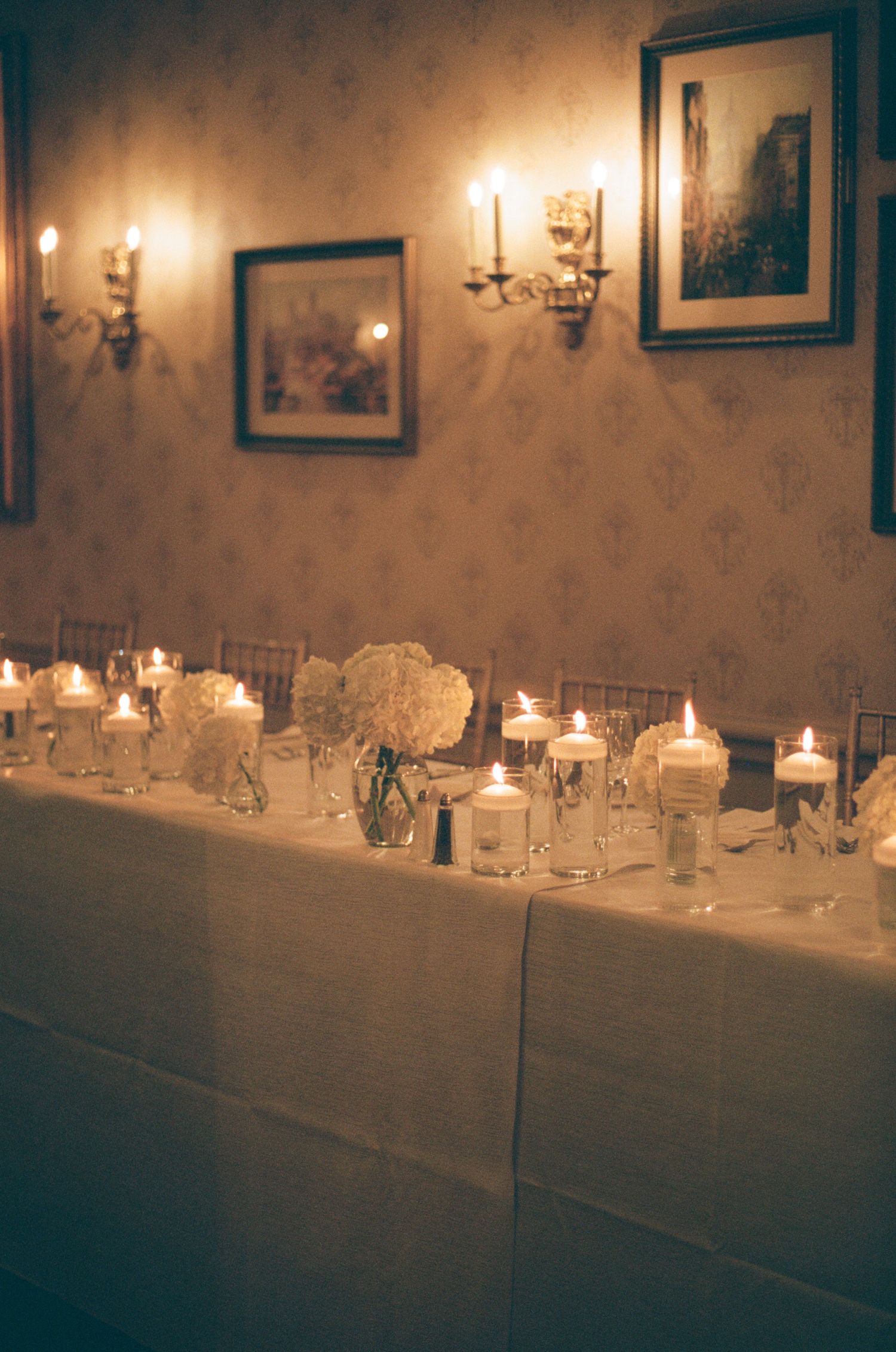 Elegant wedding reception table adorned with floating candles, white hydrangeas, and warm candlelight.