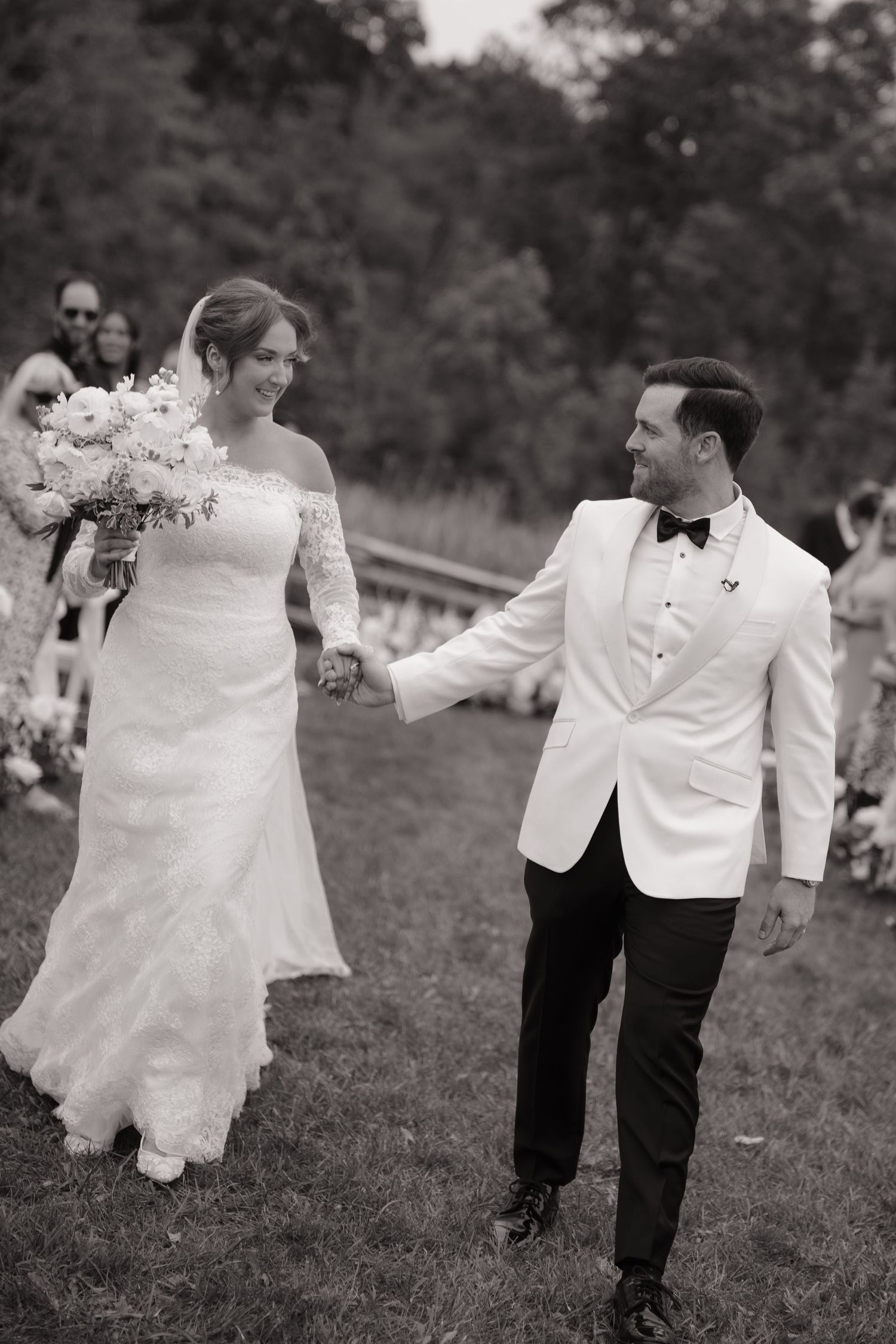 Black and white photo of newlyweds walking hand in hand after outdoor wedding ceremony.