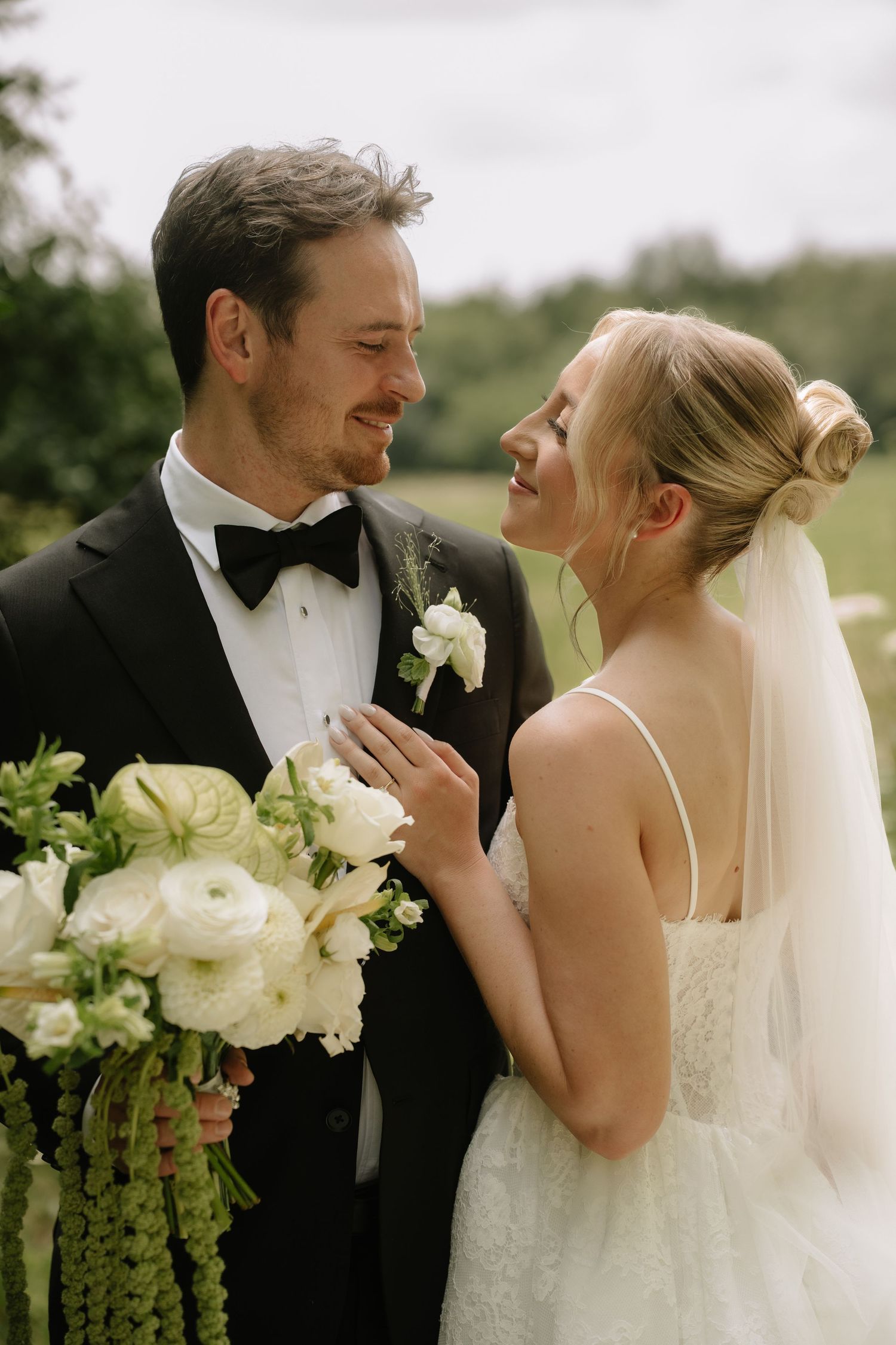 Bride and groom share a joyful moment, she in a white gown with veil, he in a black tuxedo holding a white bouquet.