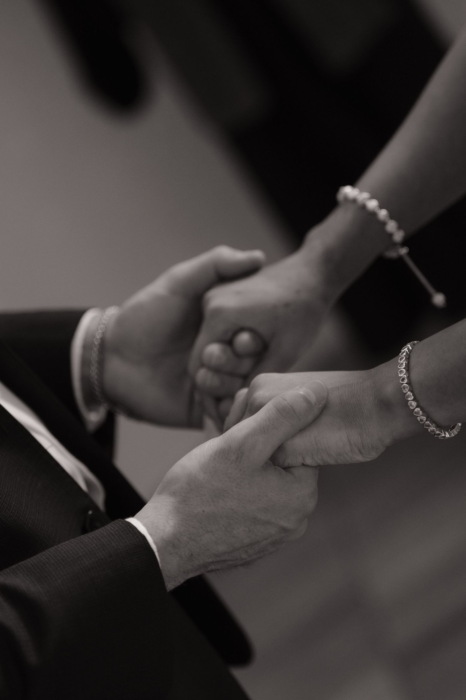 Close-up black and white image of bride and groom holding hands during wedding ceremony.