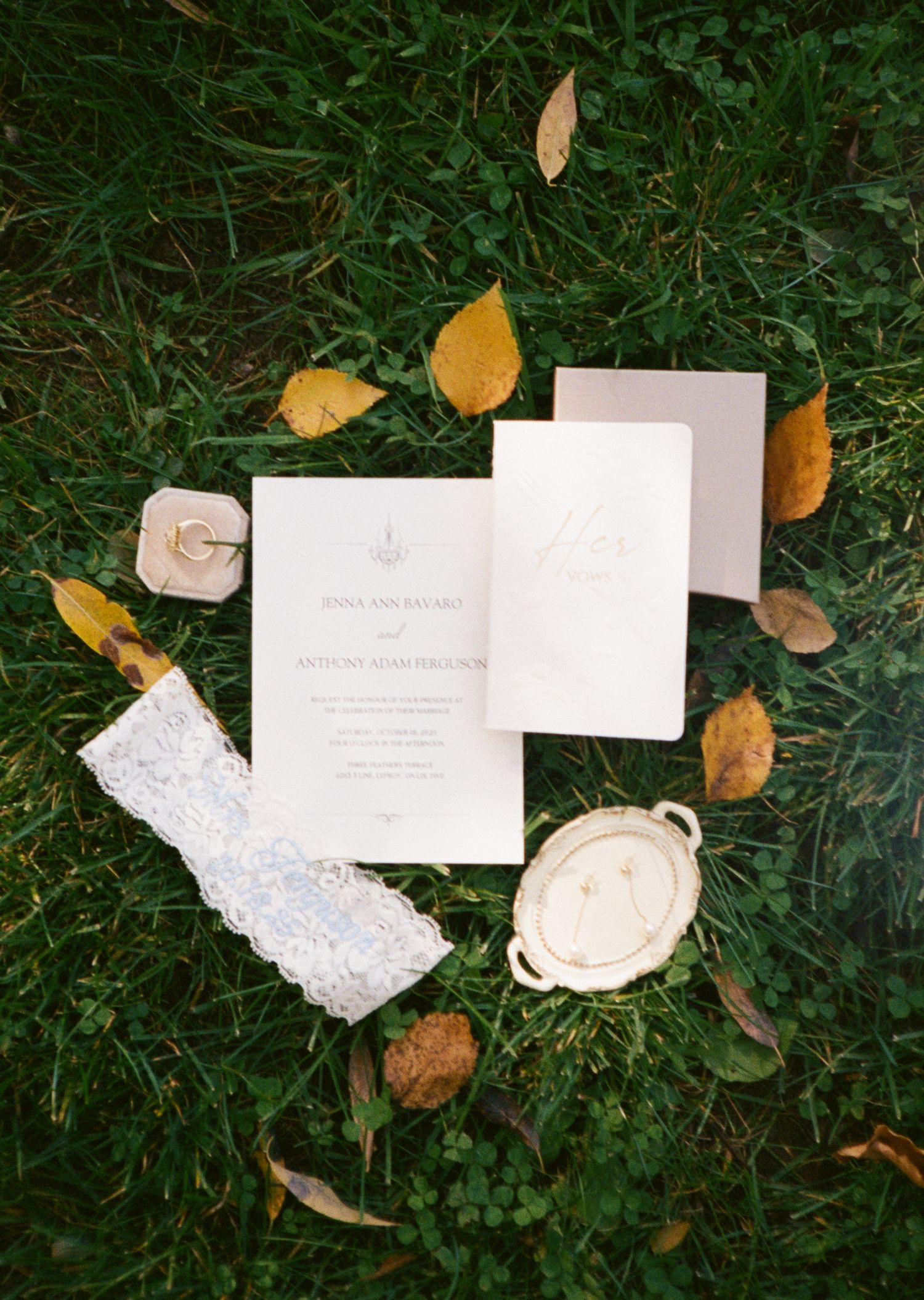 Elegant wedding invitation suite with lace garter and ring box displayed on grass with autumn leaves.