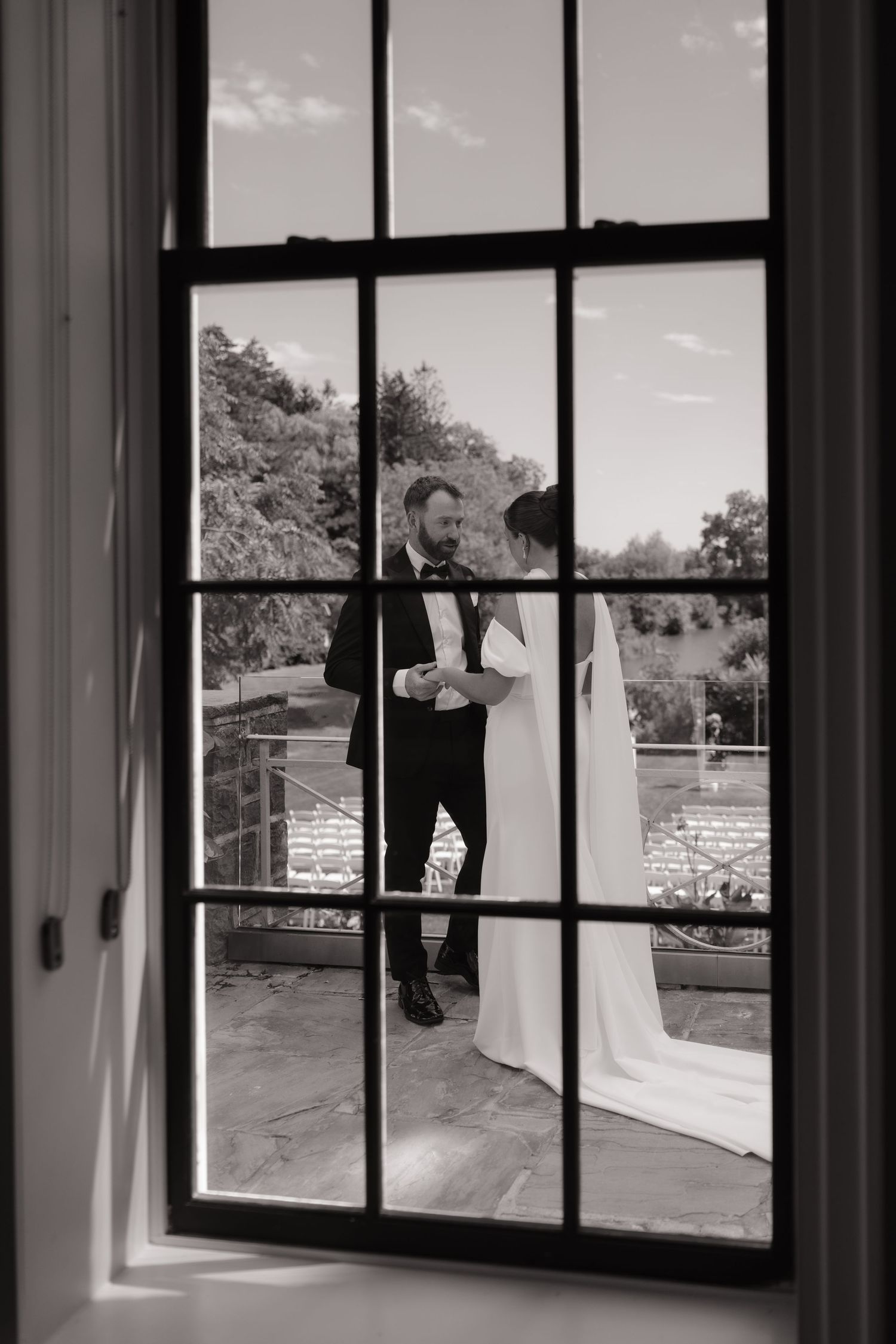 Black and white photo of bride and groom seen through elegant window panes on wedding day.