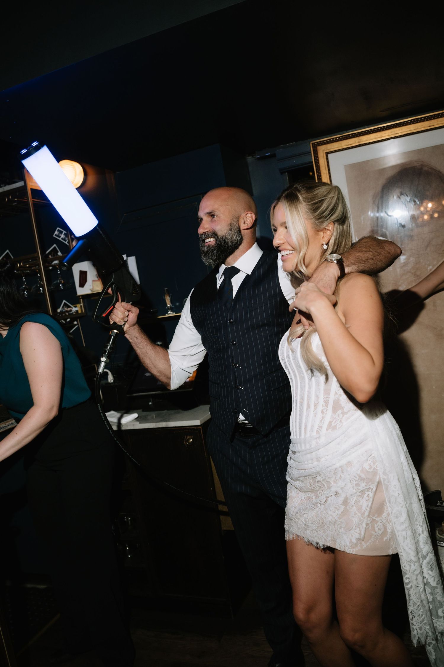 Bride in white lace dress and groom in dark vest smile together at their wedding reception party.