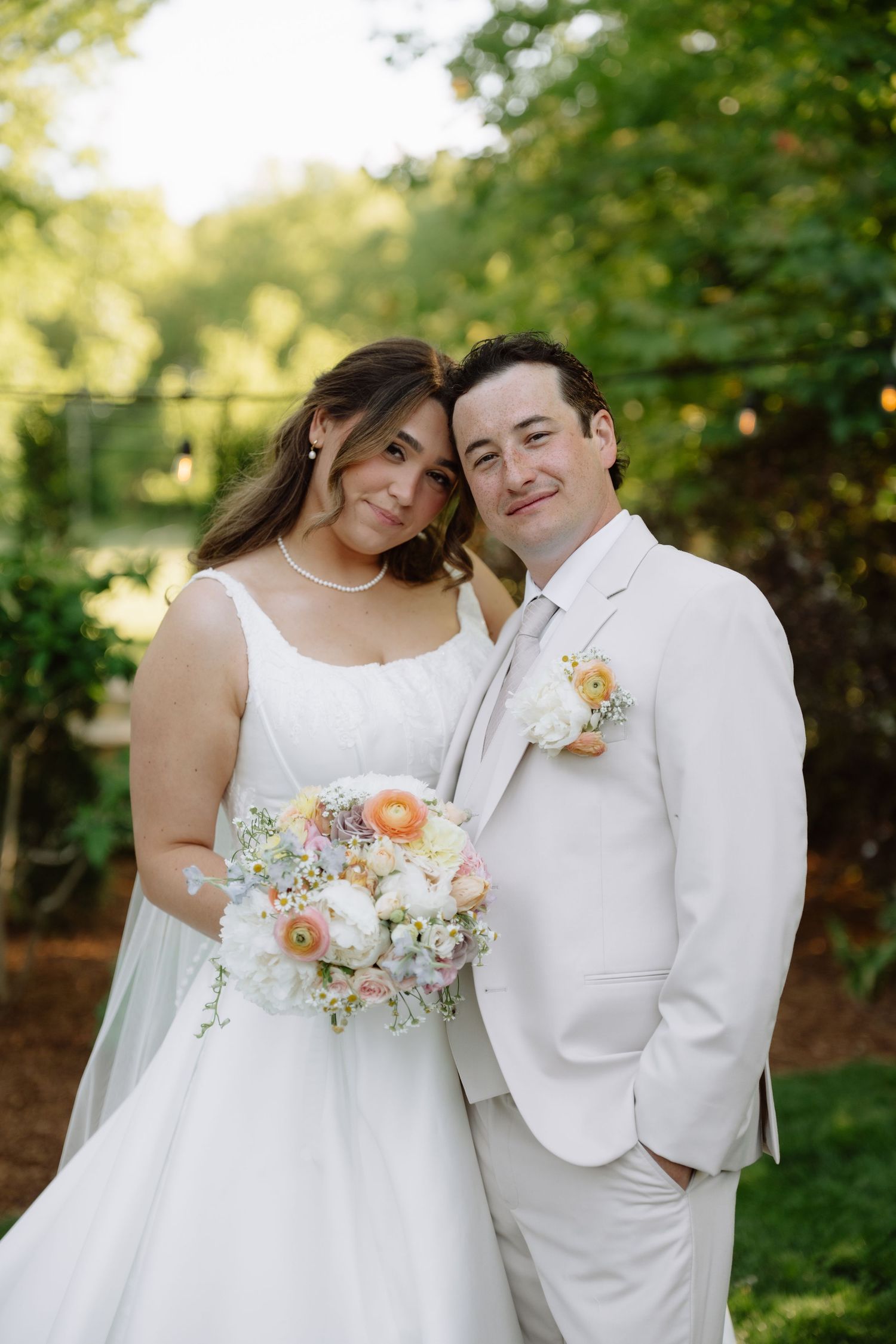 Bride and groom posing together outdoors, bride holding colorful peach and white floral bouquet.
