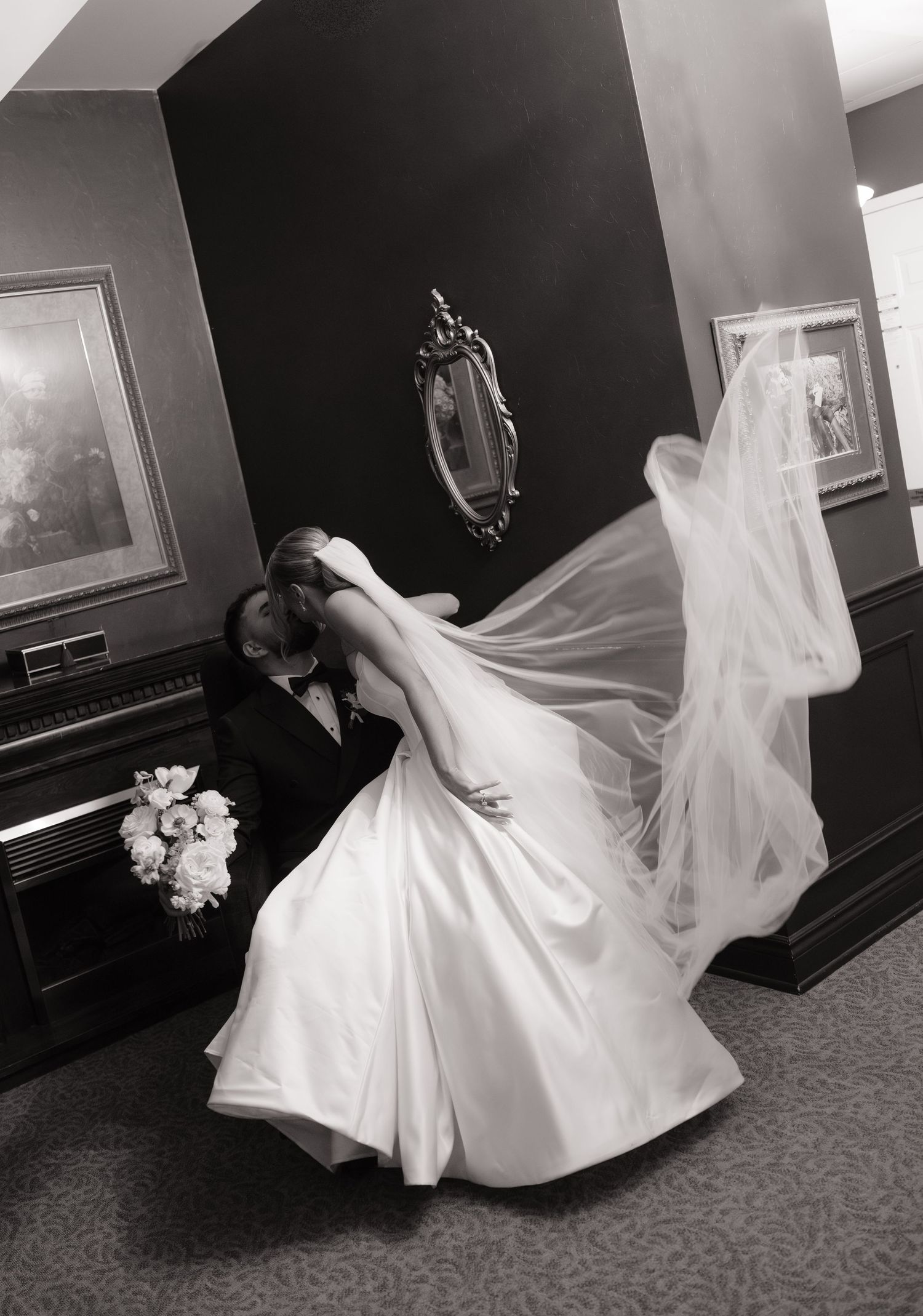 Black and white photo of bride and groom sharing a romantic dip kiss, brides veil flowing dramatically.