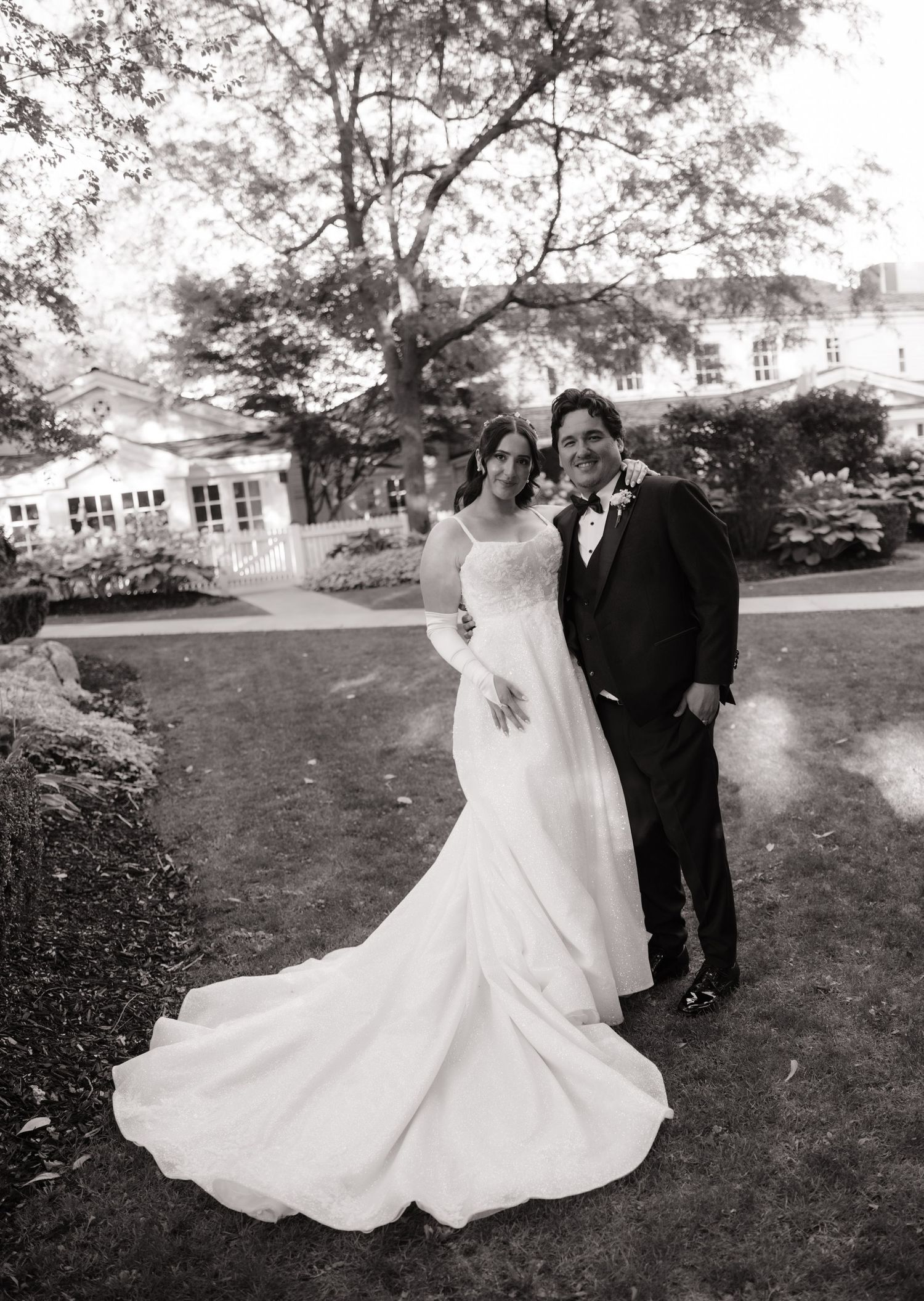 Classic black and white portrait of bride and groom on lawn before elegant estate.