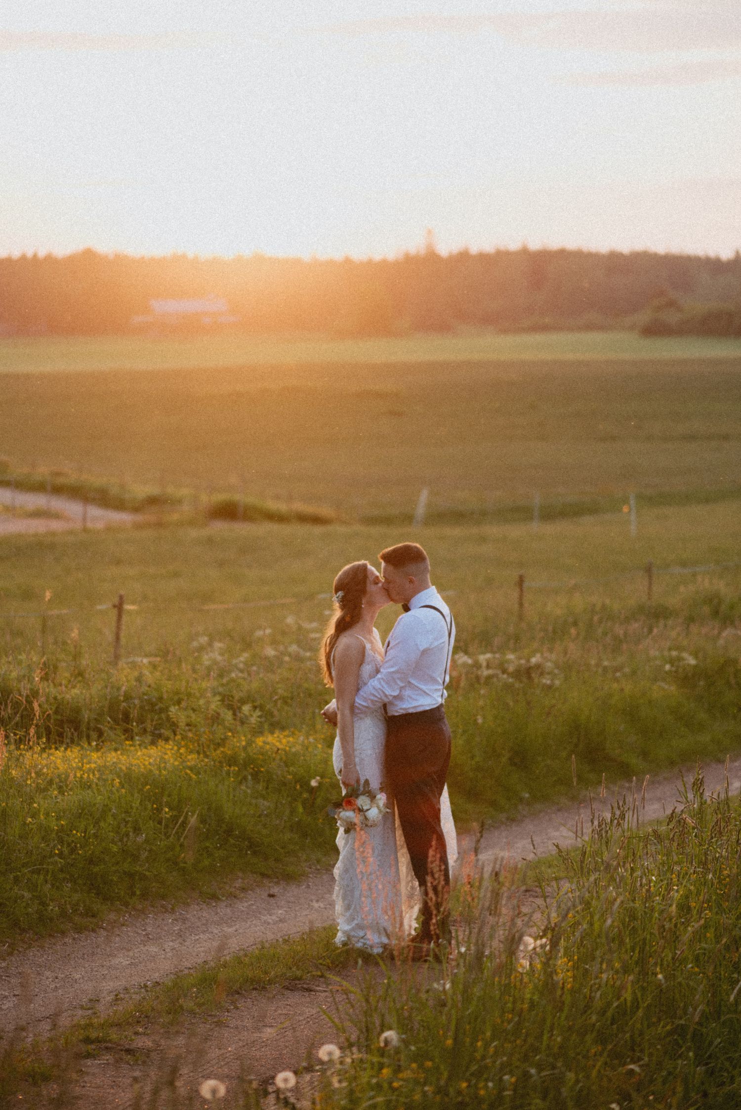 Romanttinen kuva hääparista golden hour aikaan peltomaisemassa.