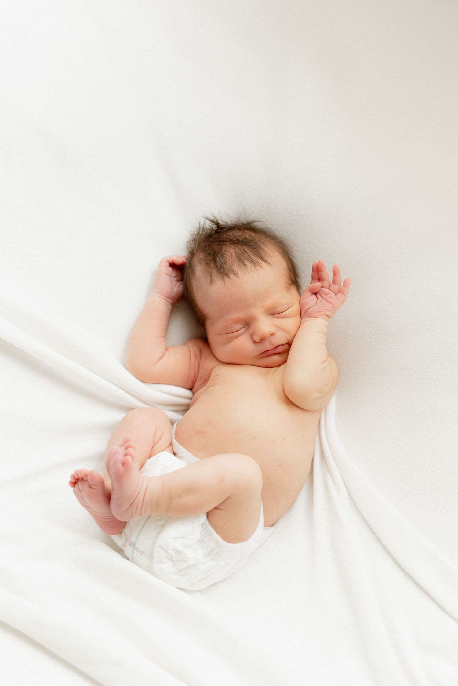 pieni newborn vastasyntynyt vauva käpertyneenä valkoisella alustalla