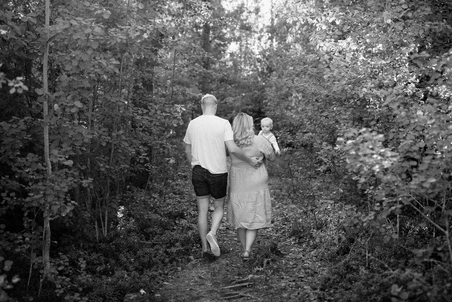 Perhe kävelee metsässä lapsi sylissä - ohjattu perhekuvaus