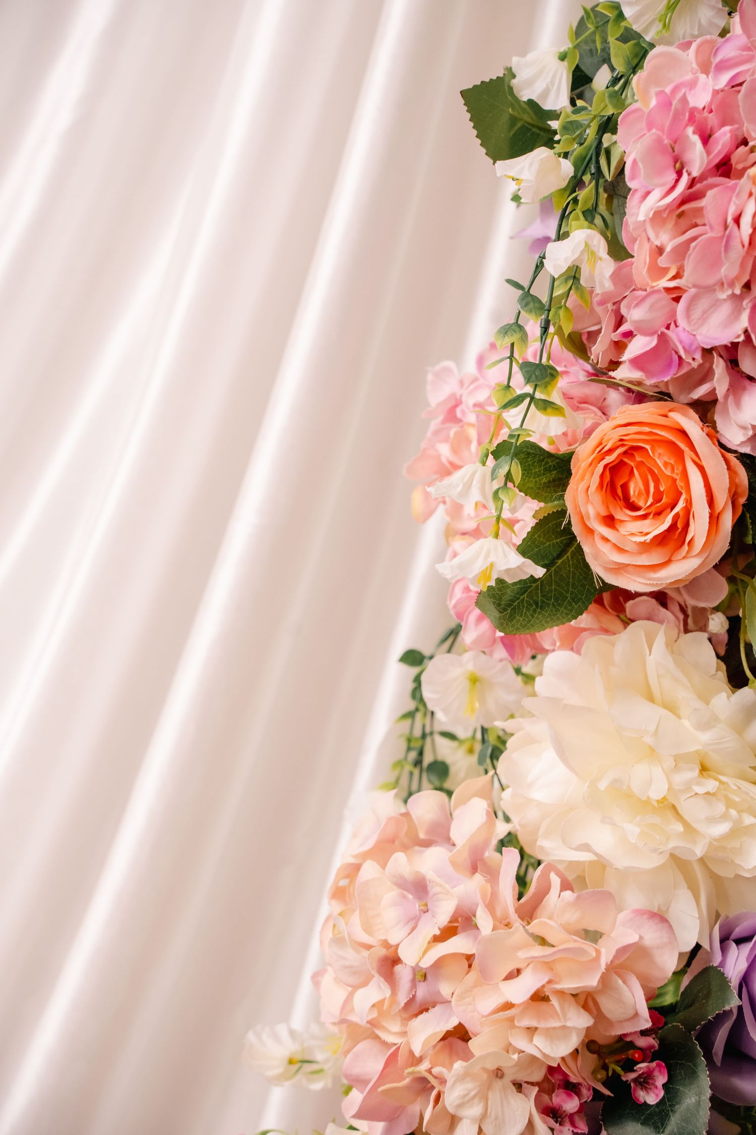 detail shot of white satin backdrop cloth and white pink and peach flowers on the border. Tied in Time Photography.