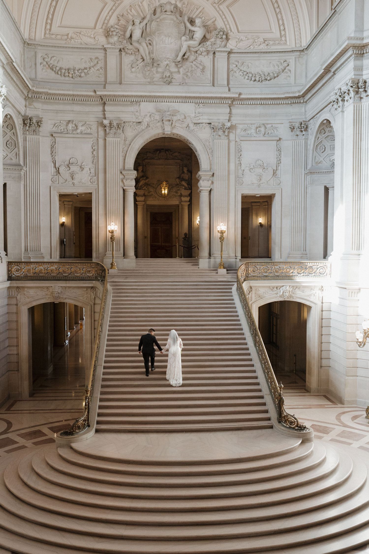 Grand marble staircase in classical building with ornate architectural details and soft lighting.