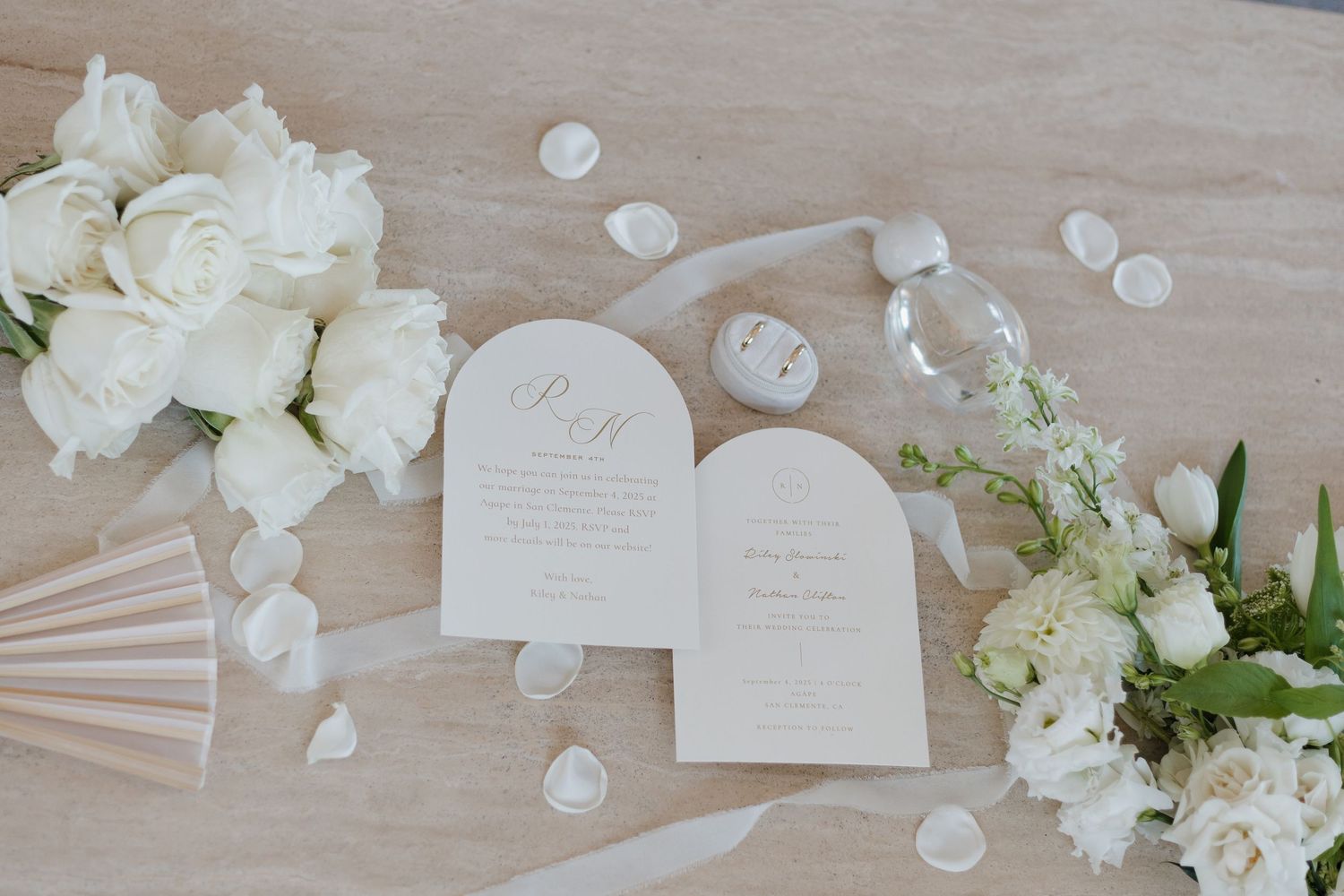 Elegant white floral arrangements and wedding stationery laid out on a light wooden surface.