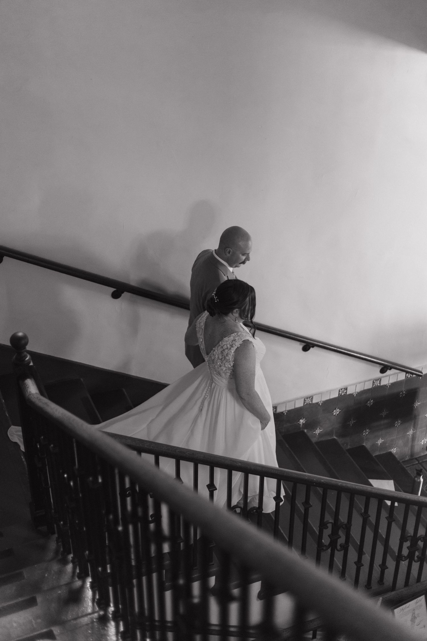 Black and white image of a bride descending a staircase with dramatic lighting.