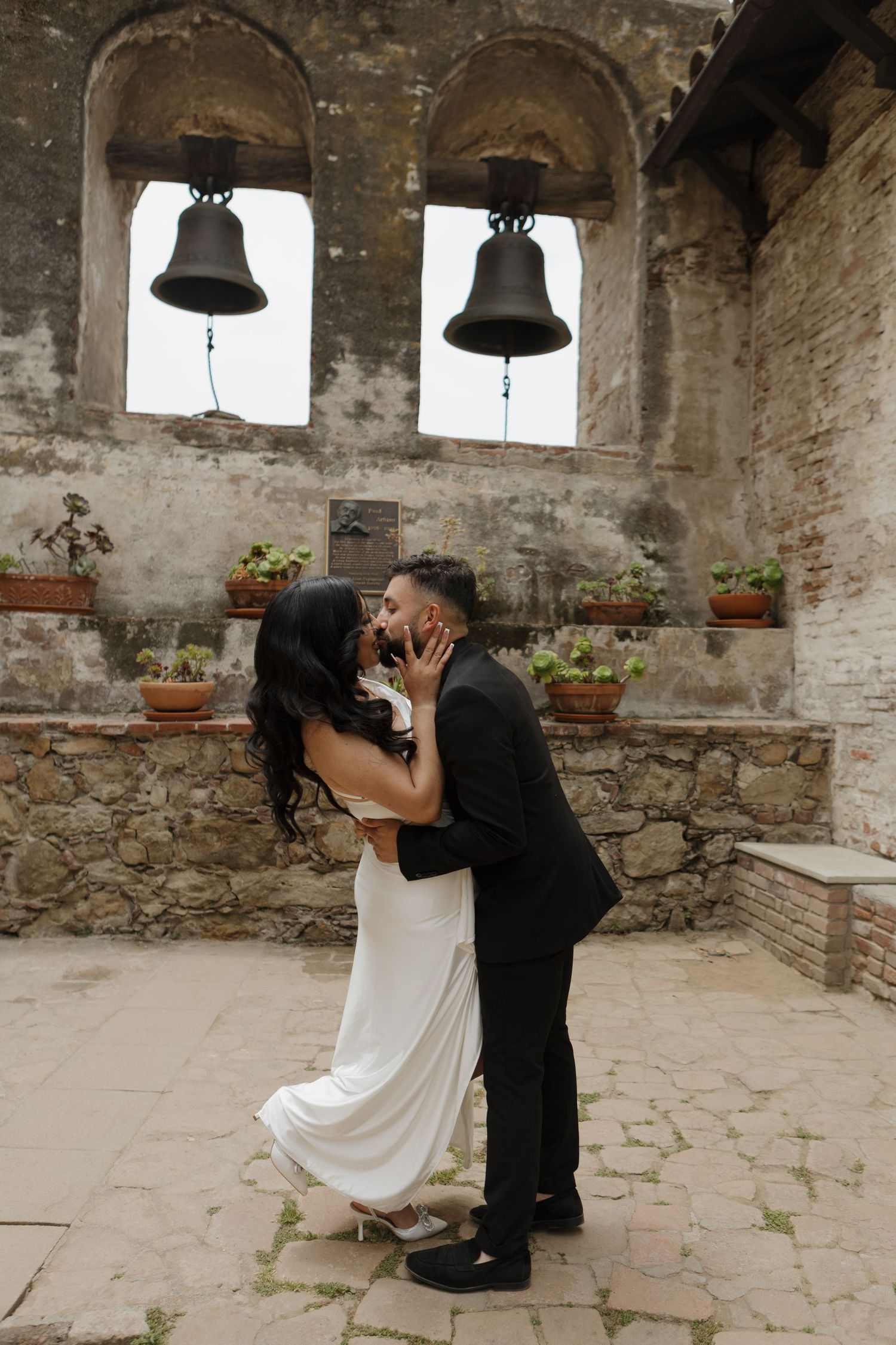 Historic stone mission with bells provides backdrop for intimate couple photos.