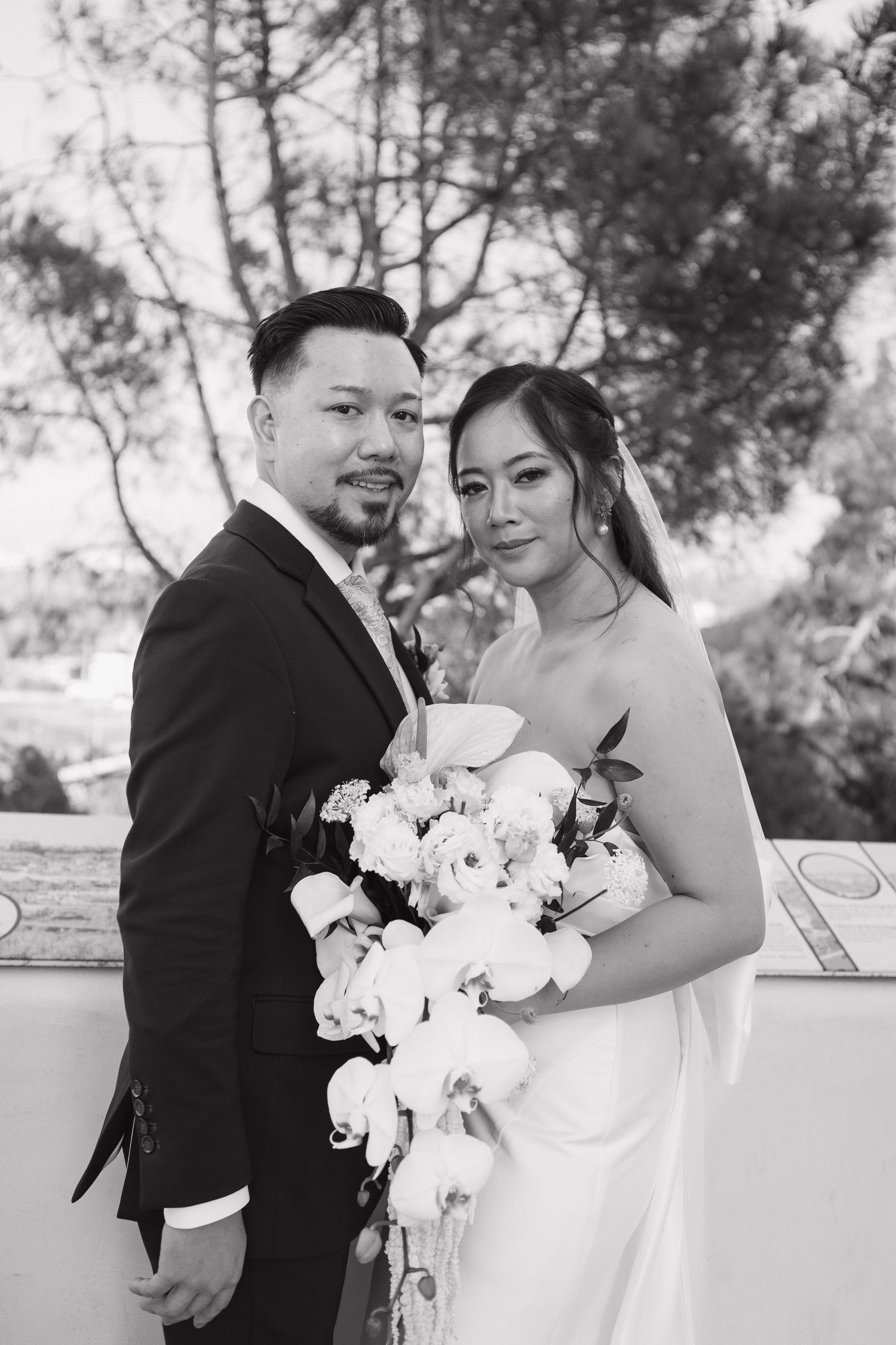 Wedding couple shares intimate moments while posing with white orchid bouquet.