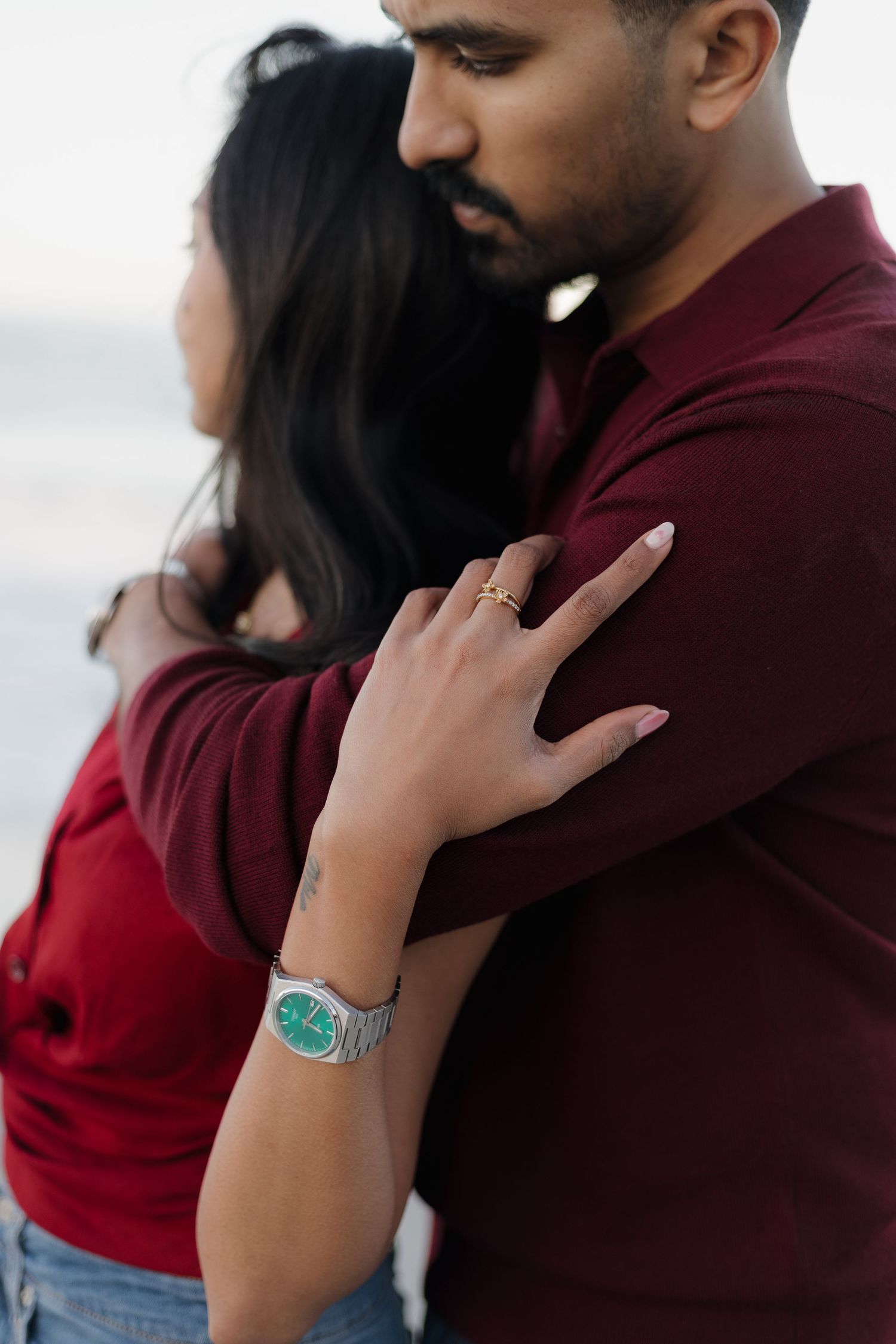 Close-up of hands embracing in burgundy sweater showing turquoise watch detail.