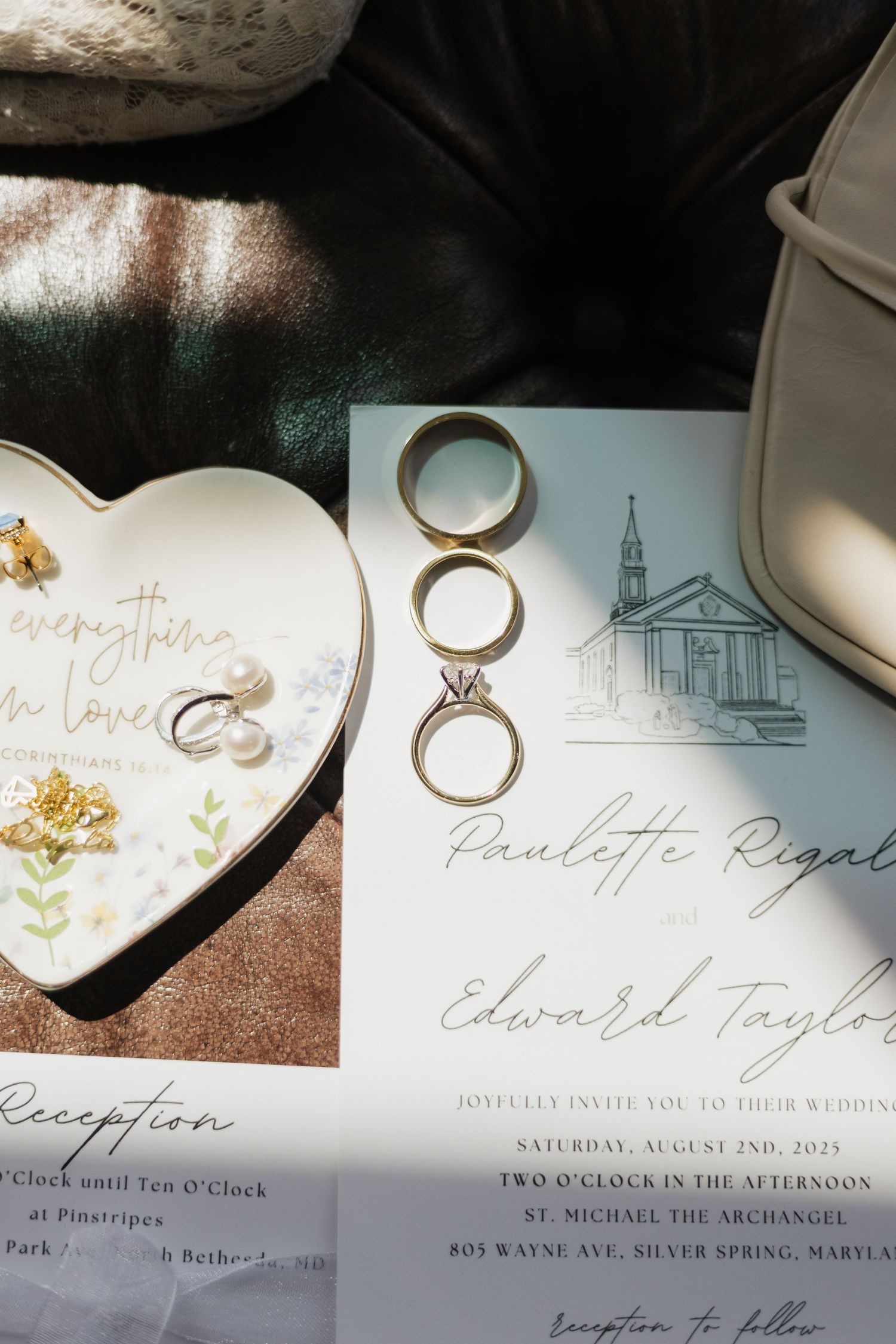 Wedding invitation for Paulette Rigal and Edward Taylor with gold rings, earrings, and a heart-shaped jewelry dish on a elegant flat lay.