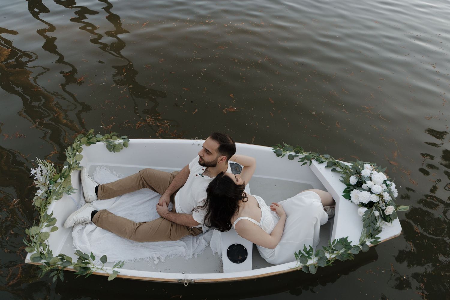 Couple shares intimate moment in a small white rowboat on calm waters.