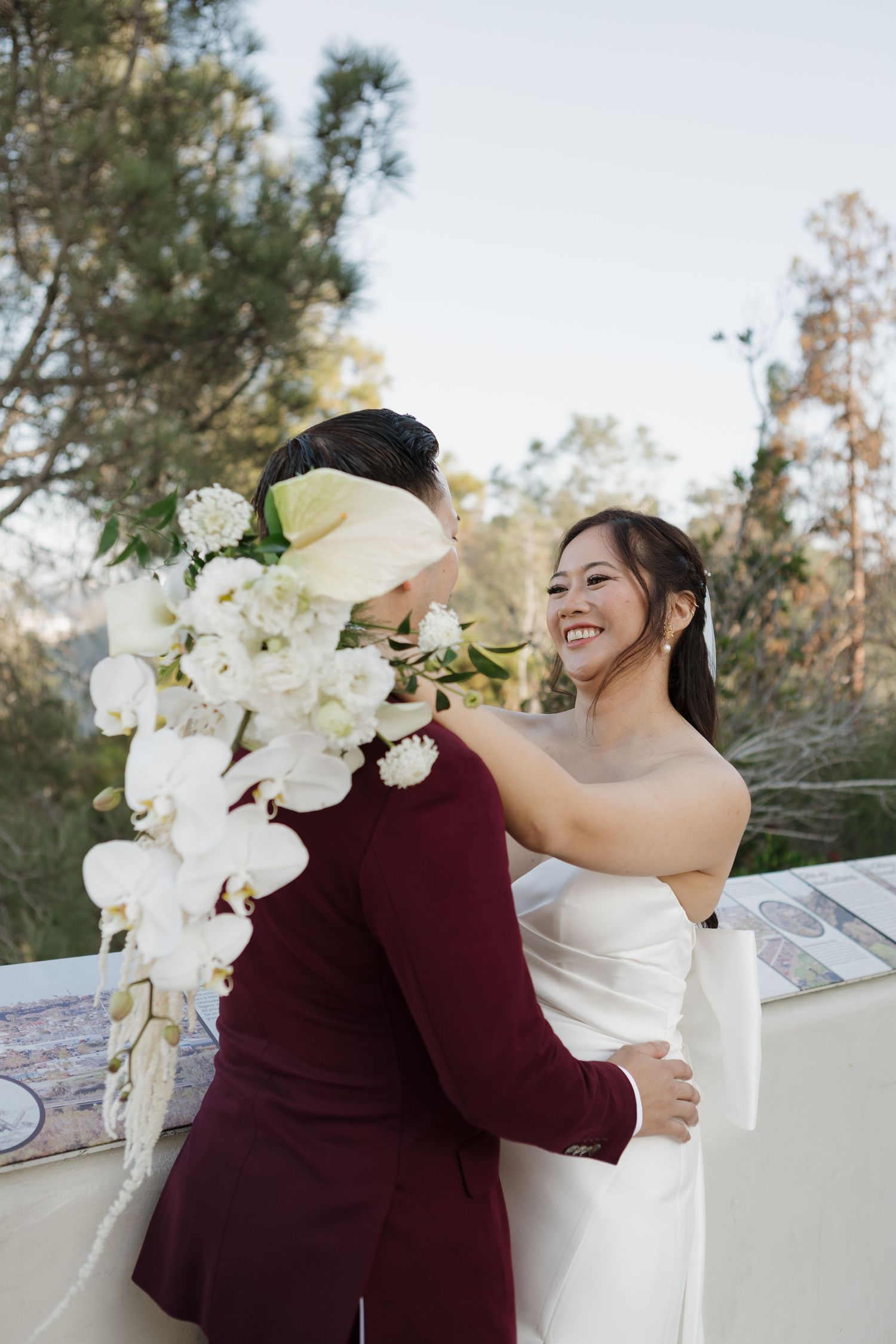 A joyful embrace with white orchid bouquet against an outdoor backdrop.