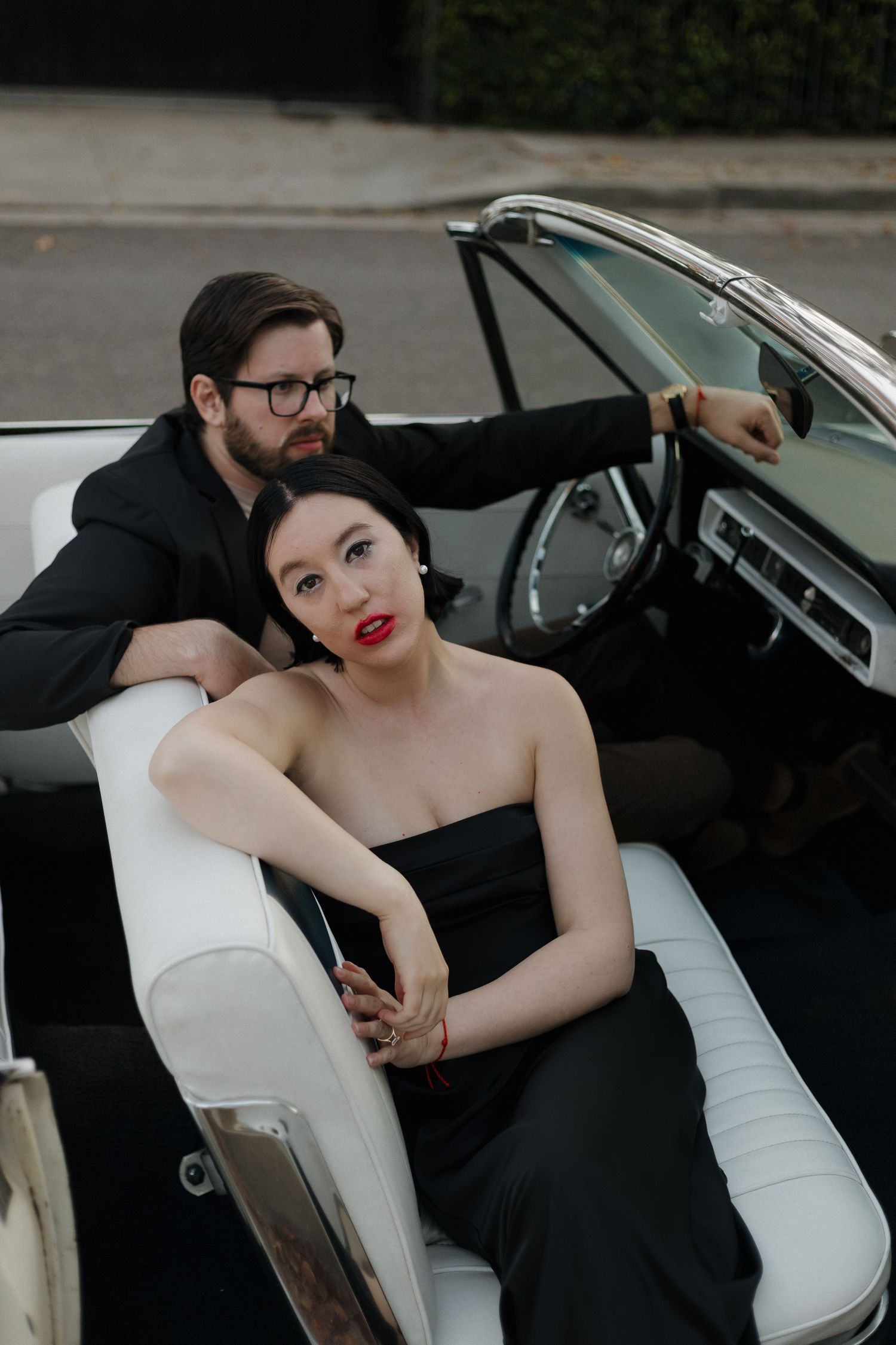 Glamorous couple posing dramatically in vintage car interior.