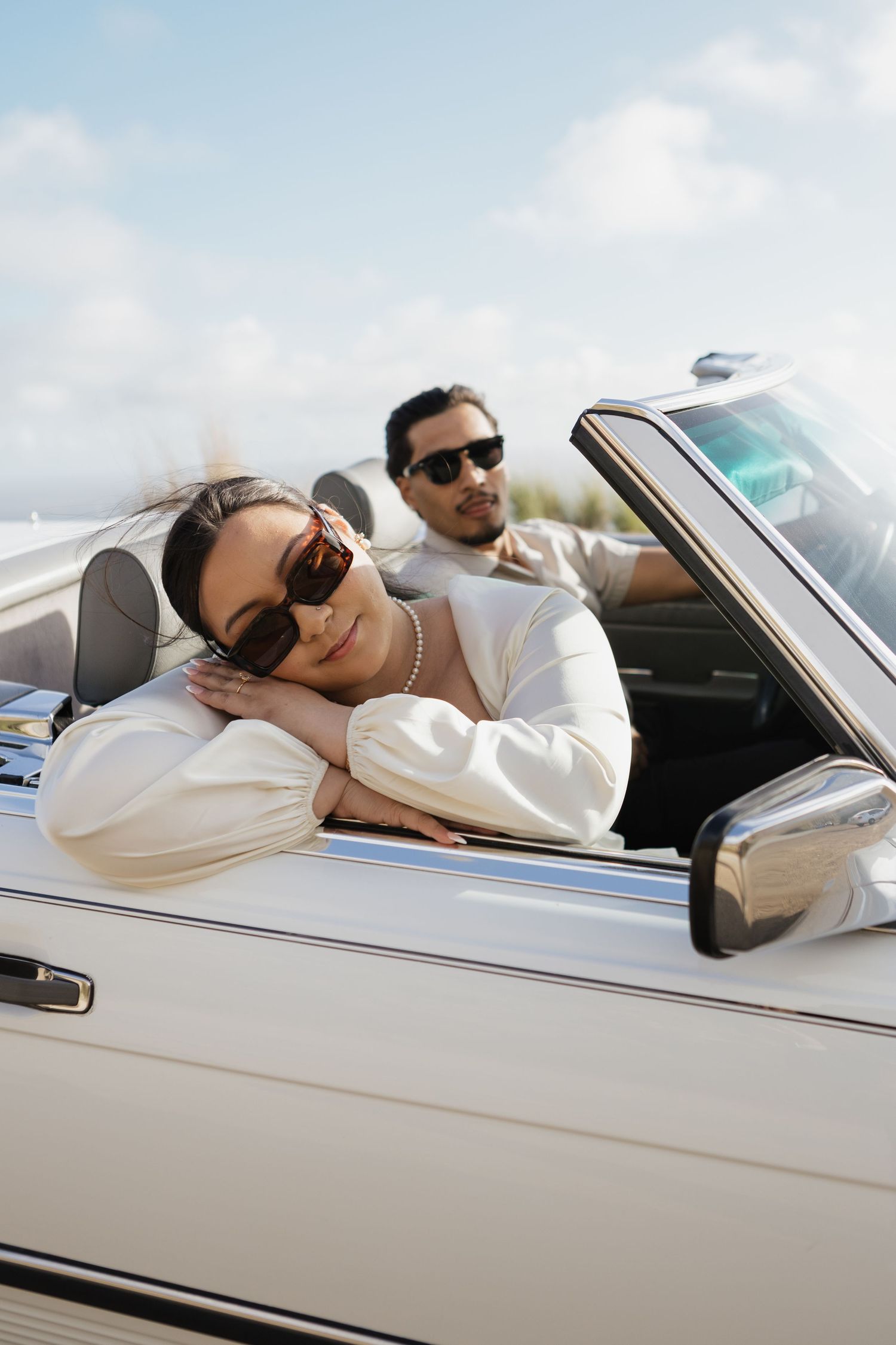 Couple relaxing in a classic white convertible car on a sunny day.