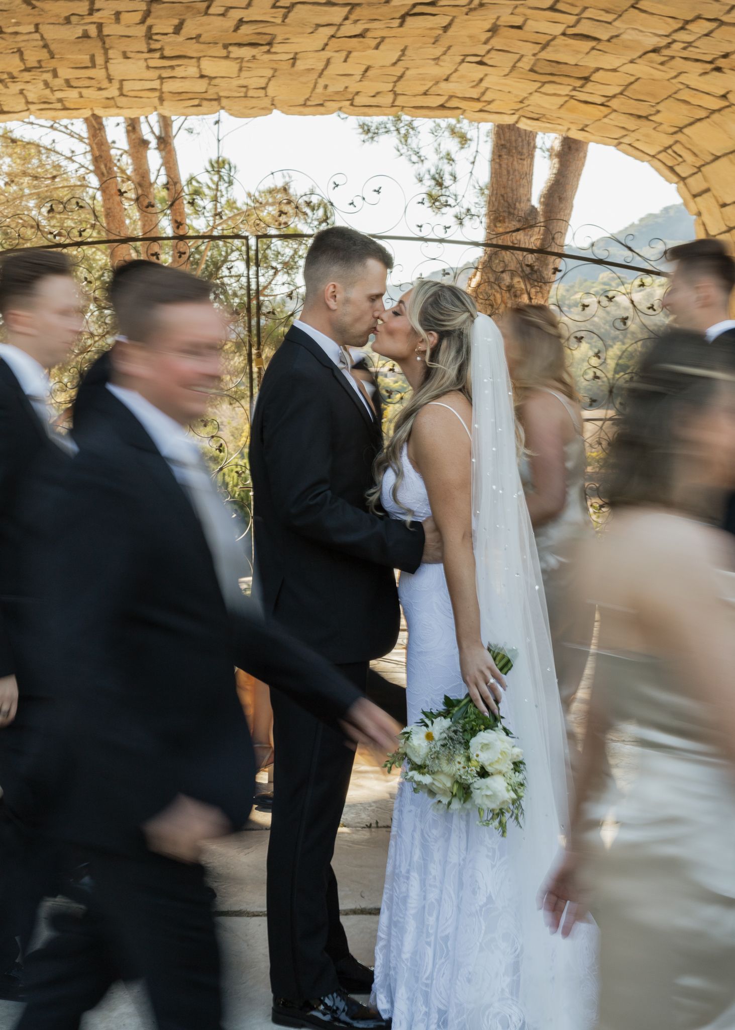 Motion-blur photo of wedding reception under stone archway with guests dancing.